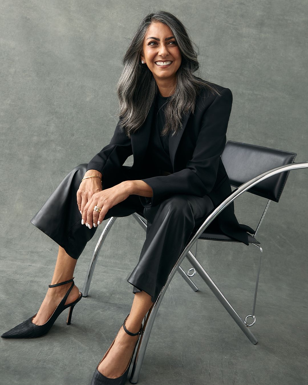 Shirley Chowdhary sitting in chair wearing Black Tailored Jacket and Black Leather Trousers