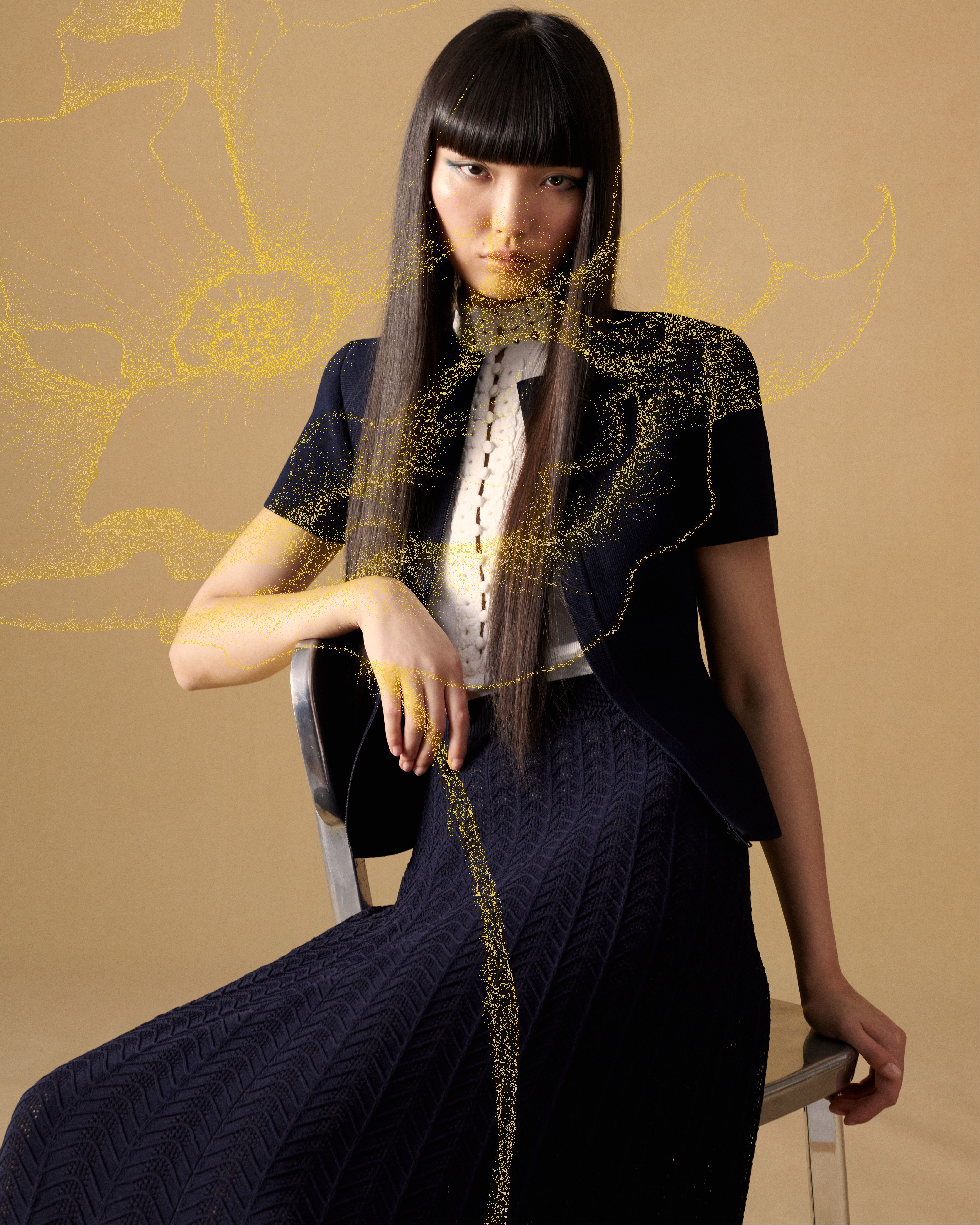 Model sitting in chair wearing navy a Crepe Knit jacket and skirt with a yellow poppy illustration overlaid on top
