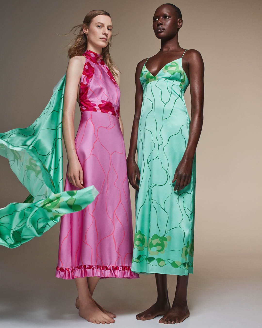 Julia Nobis wearing a pink silk halterneck dress standing with Ajak Deng wearing a green silk dress