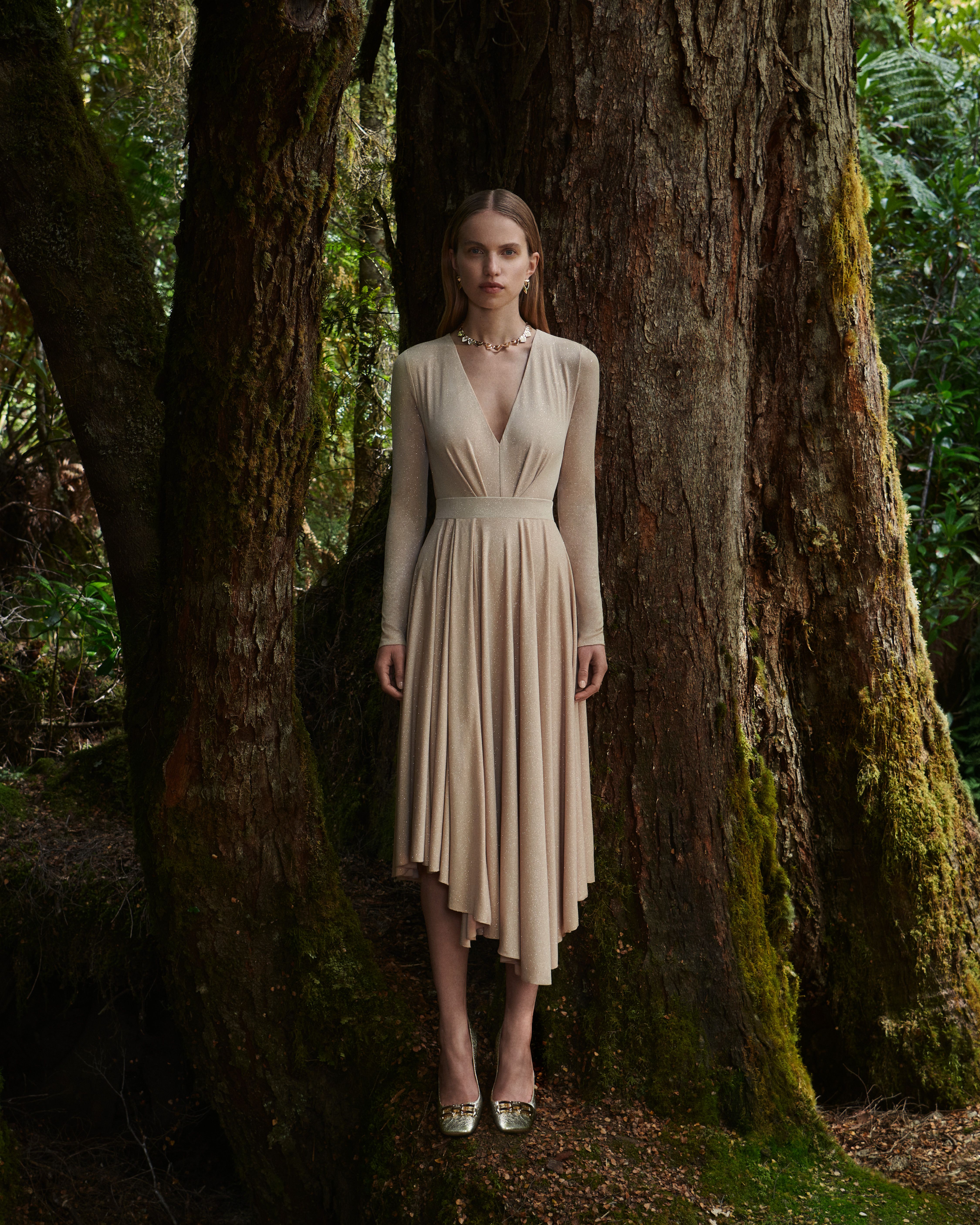 Sabine Glud standing in the forest wearing a beige v-neck top and skirt.