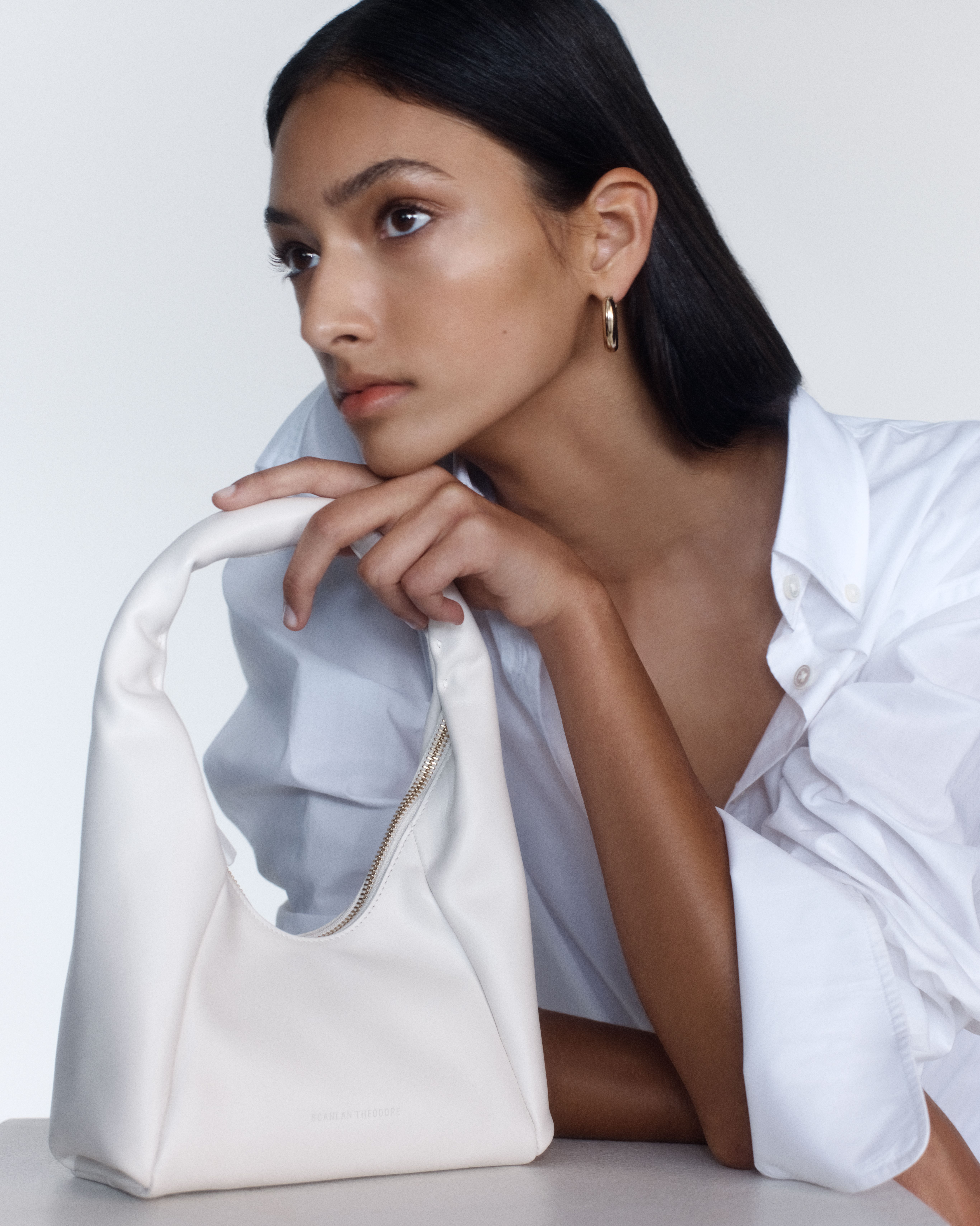 Model leaning on bench resting her hand and chin on a small white leather bag