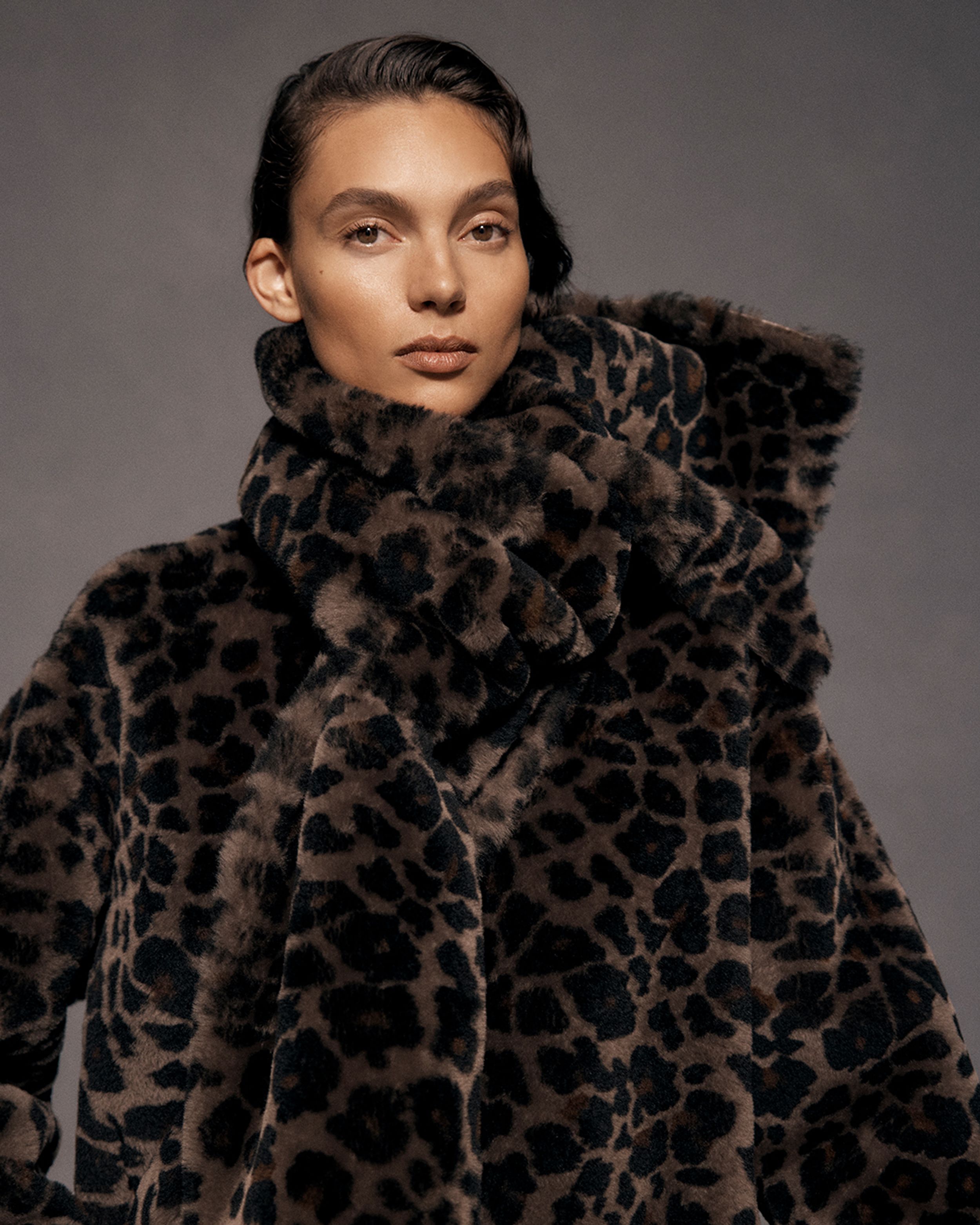 Close up of brunette model wearing a matching leopard-print coat and scarf