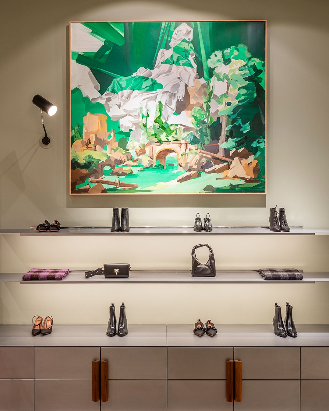 Display shelves of shoes and boots with painting hanging above depicting mountain covered in greenery and stone