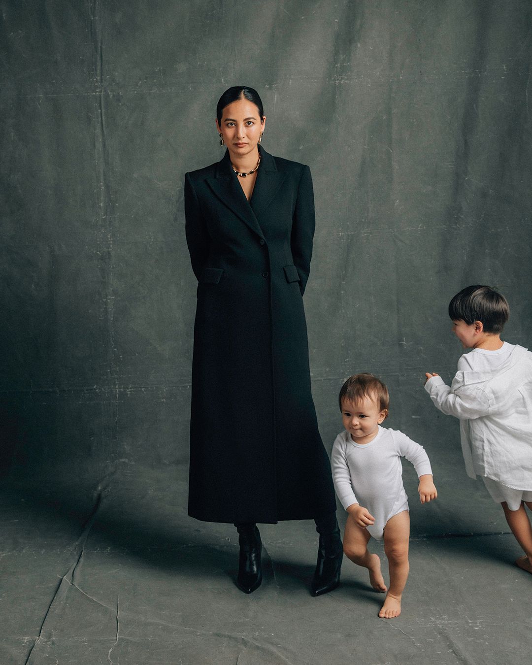 Petta Chua standing in a long black coat with her two sons running around