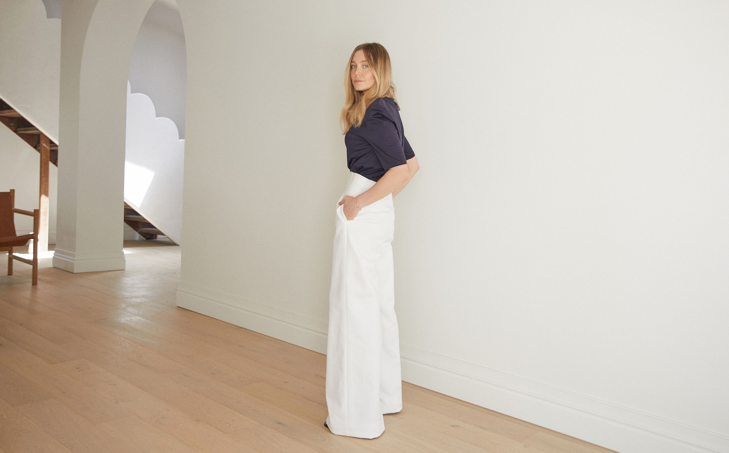 Hayley Bonham wearing white wide leg trousers and a short sleeve top standing with her hands in the trouser pockets