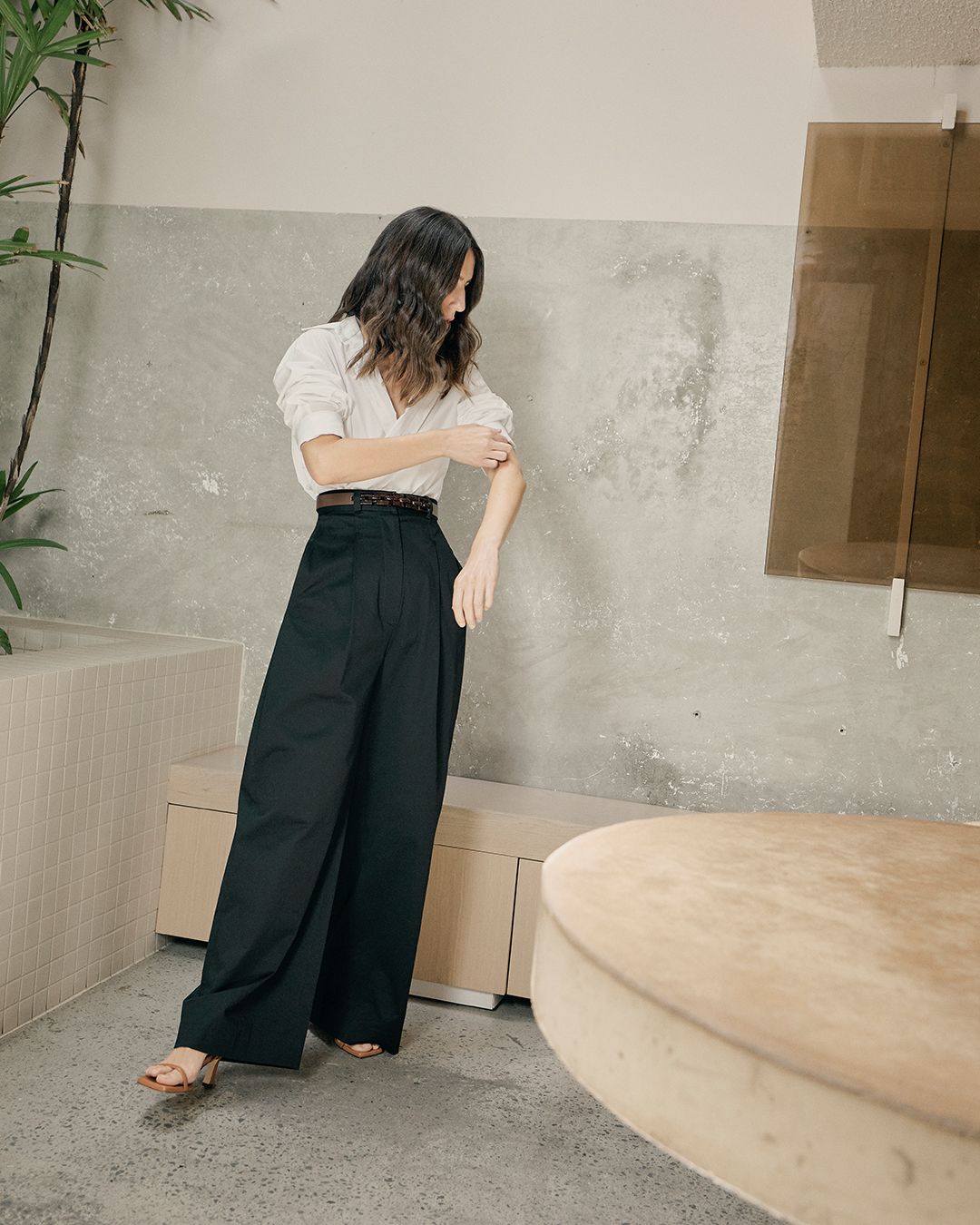Bianca Marchi wearing a white shirt and black wide leg trousers candidly adjusting her sleeve
