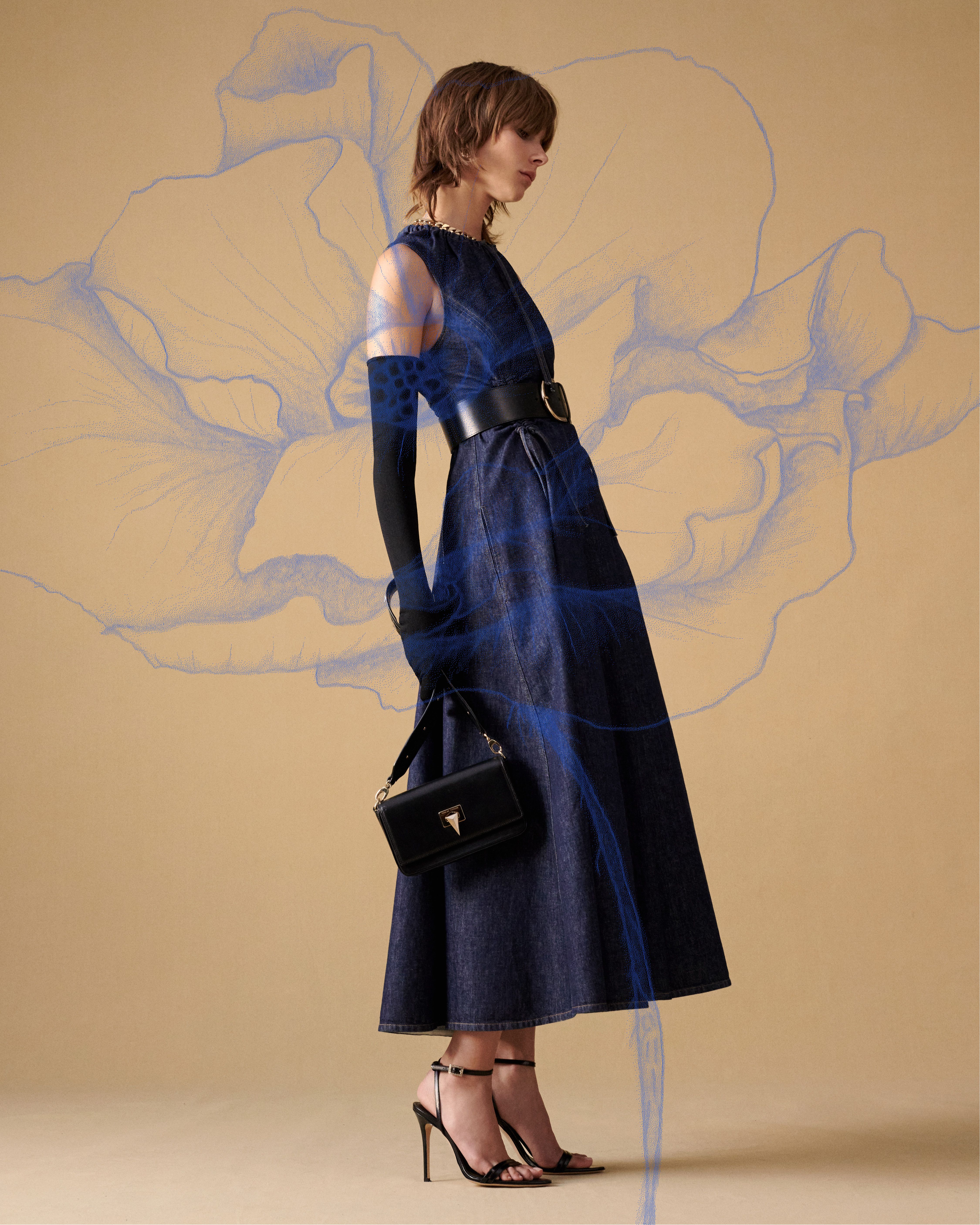 Model facing the side wearing a long denim dress with black gloves and bag with blue poppy illustration overlaid on top
