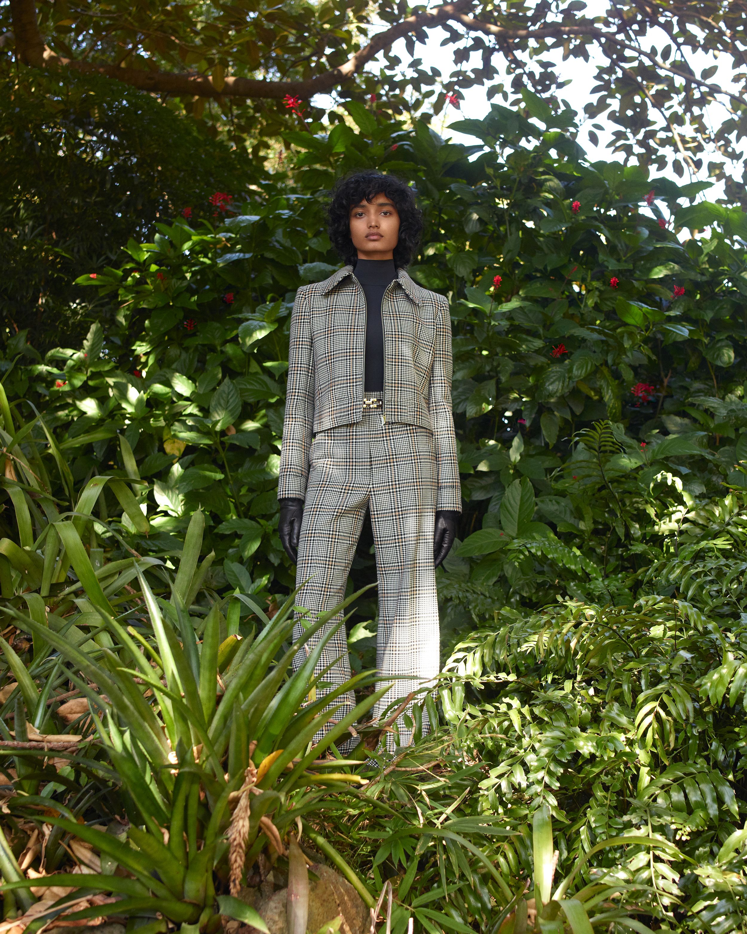 Model standing amongst dense greenery wearing a matching grey plaid jacket and trousers