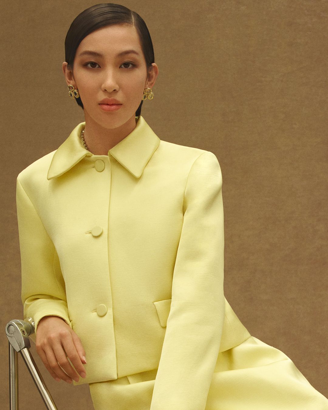 Model sitting on chair wearing a yellow collared jacket and skirt