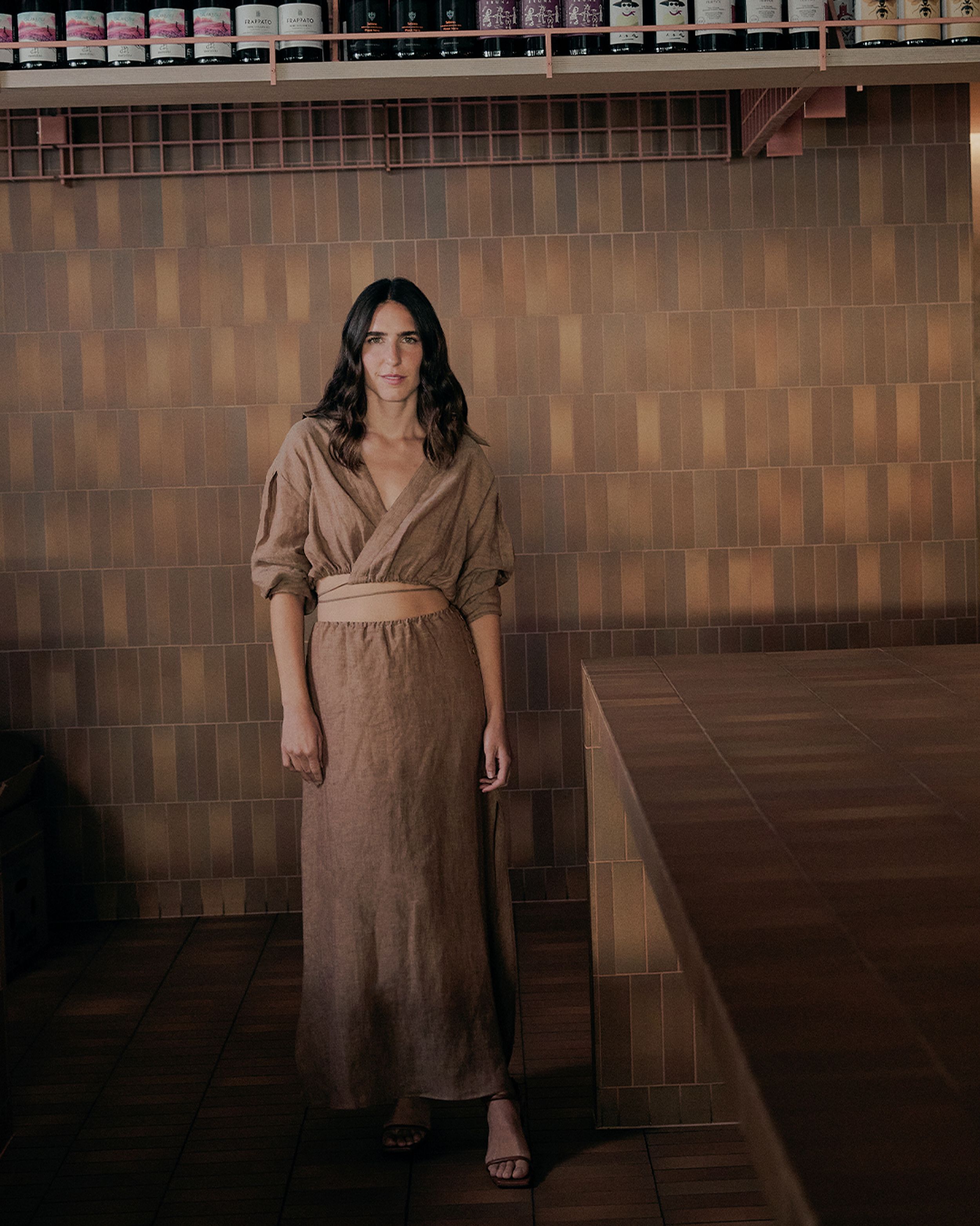 Bianca Marchi posing in front of a brown tiled wall wearing a brown linen shirt and maxi skirt