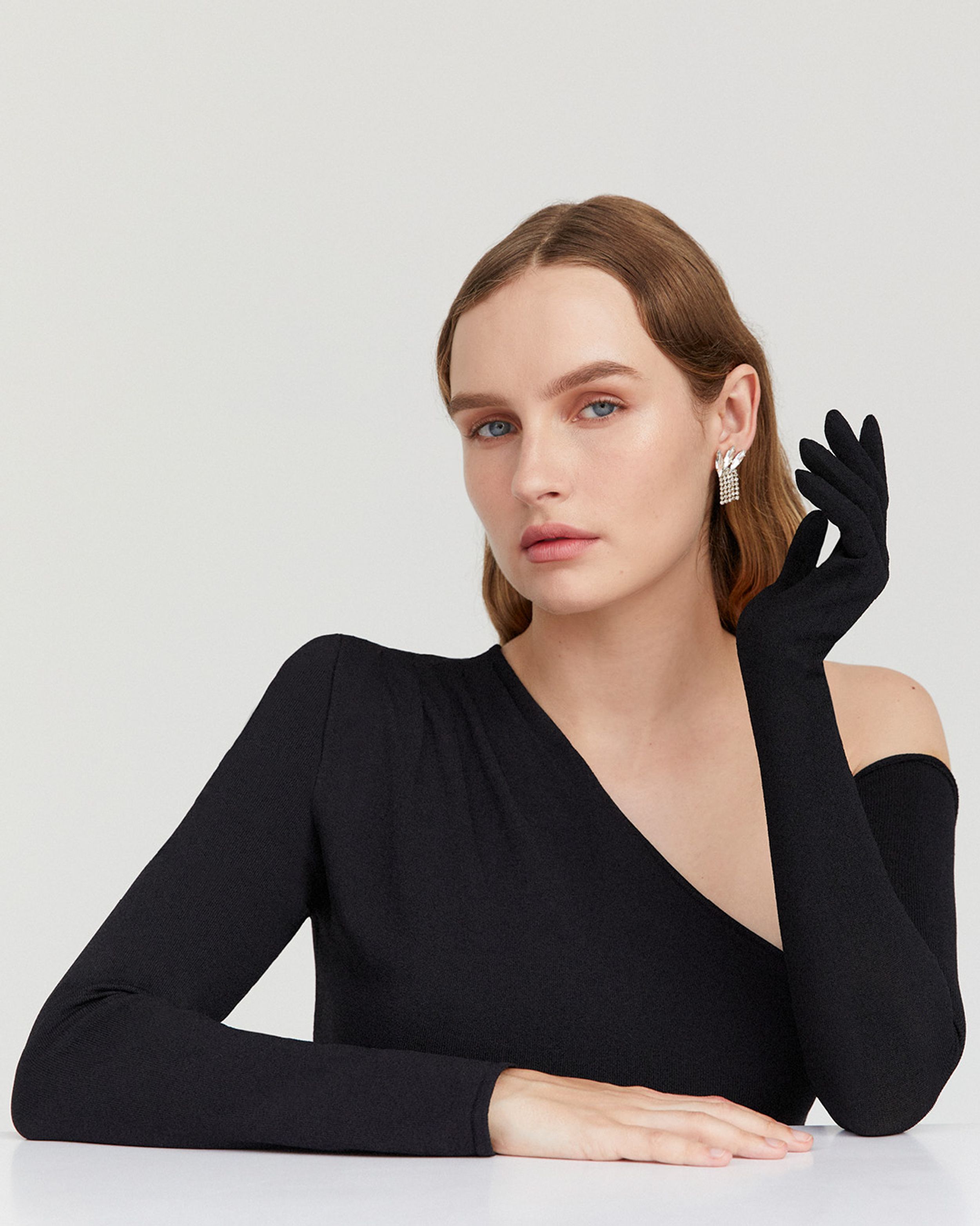 Olivia DeJonge wearing a black one-shouldered gown and black glove with hand by ear
