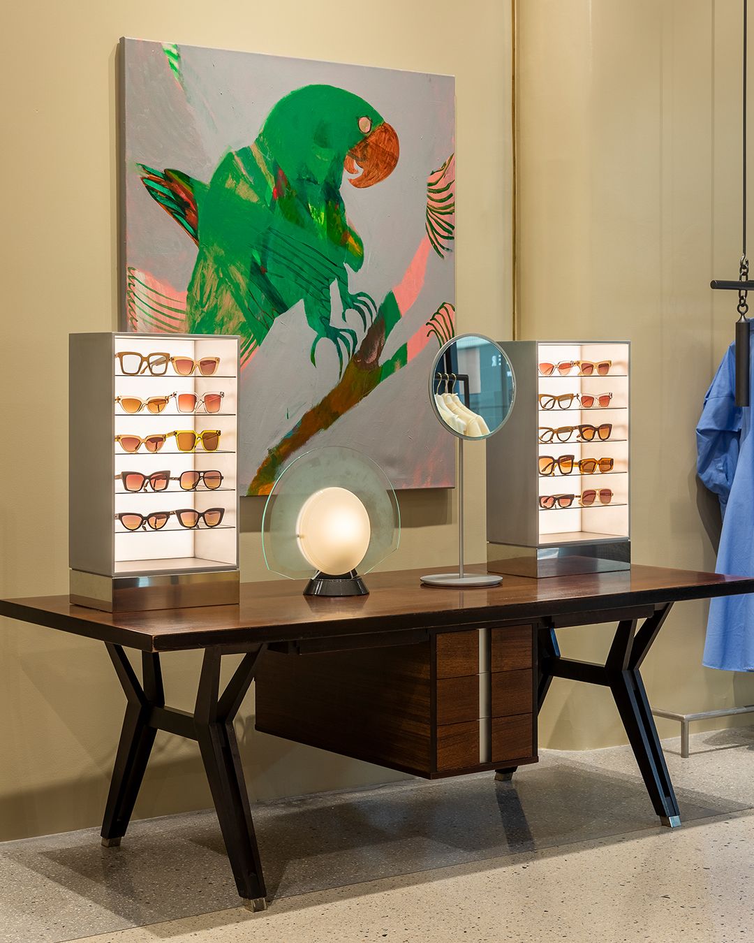 Sunglasses display on top of table with large painting of green parrot on the wall behind