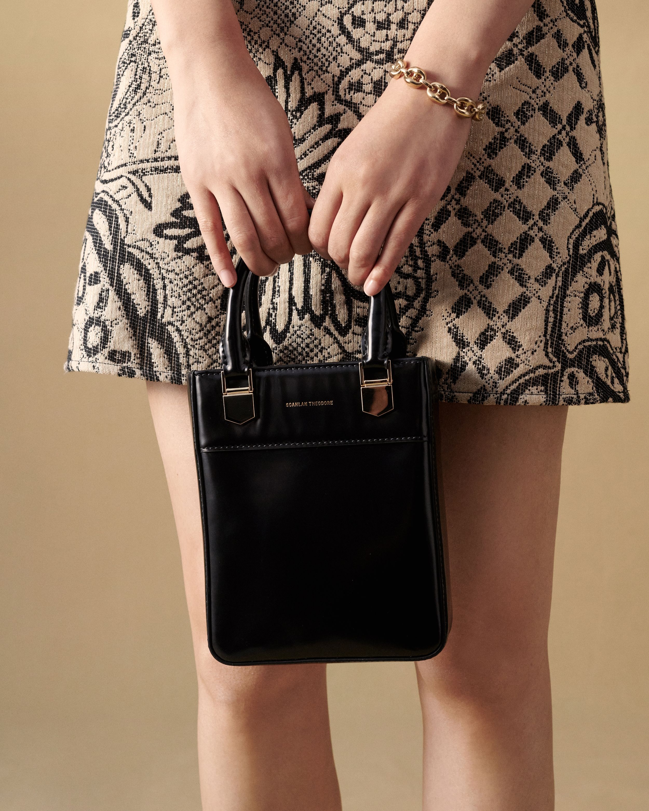 Close up shot of model holding a mini black leather bag wearing a patterned mini skirt