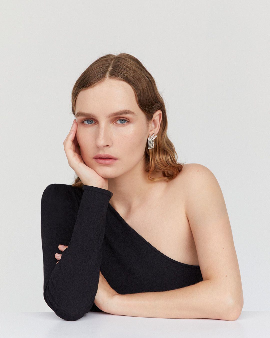 Olivia DeJonge with hand on chin wearing a black one-shouldered gown and black glove