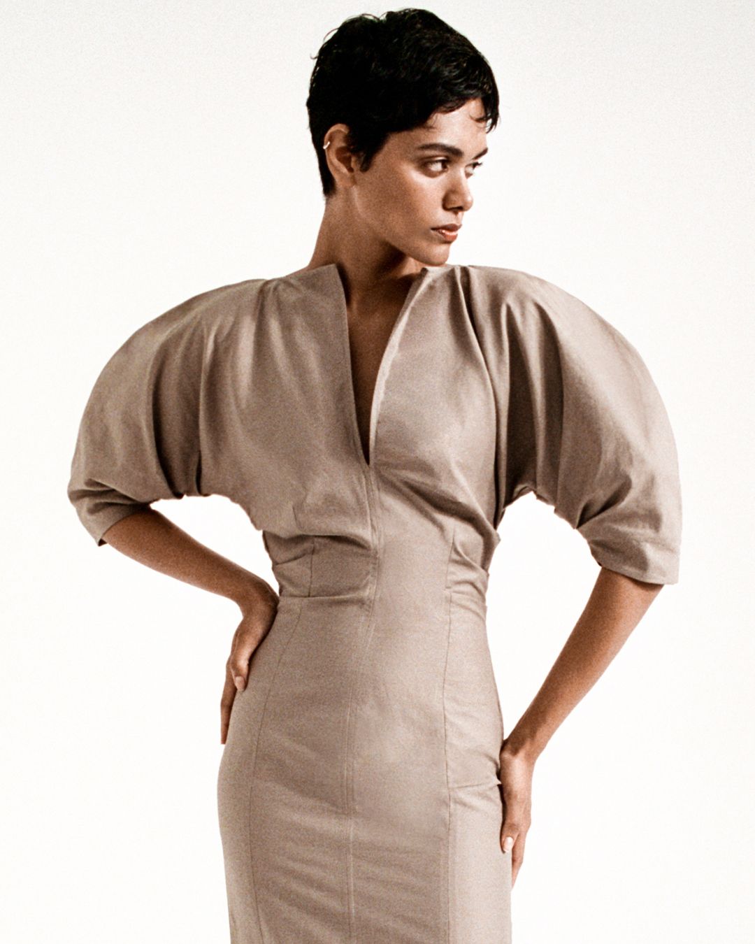 Zinnia Kumar posing with hands on hips in a fitted taupe dress with voluminous sleeves