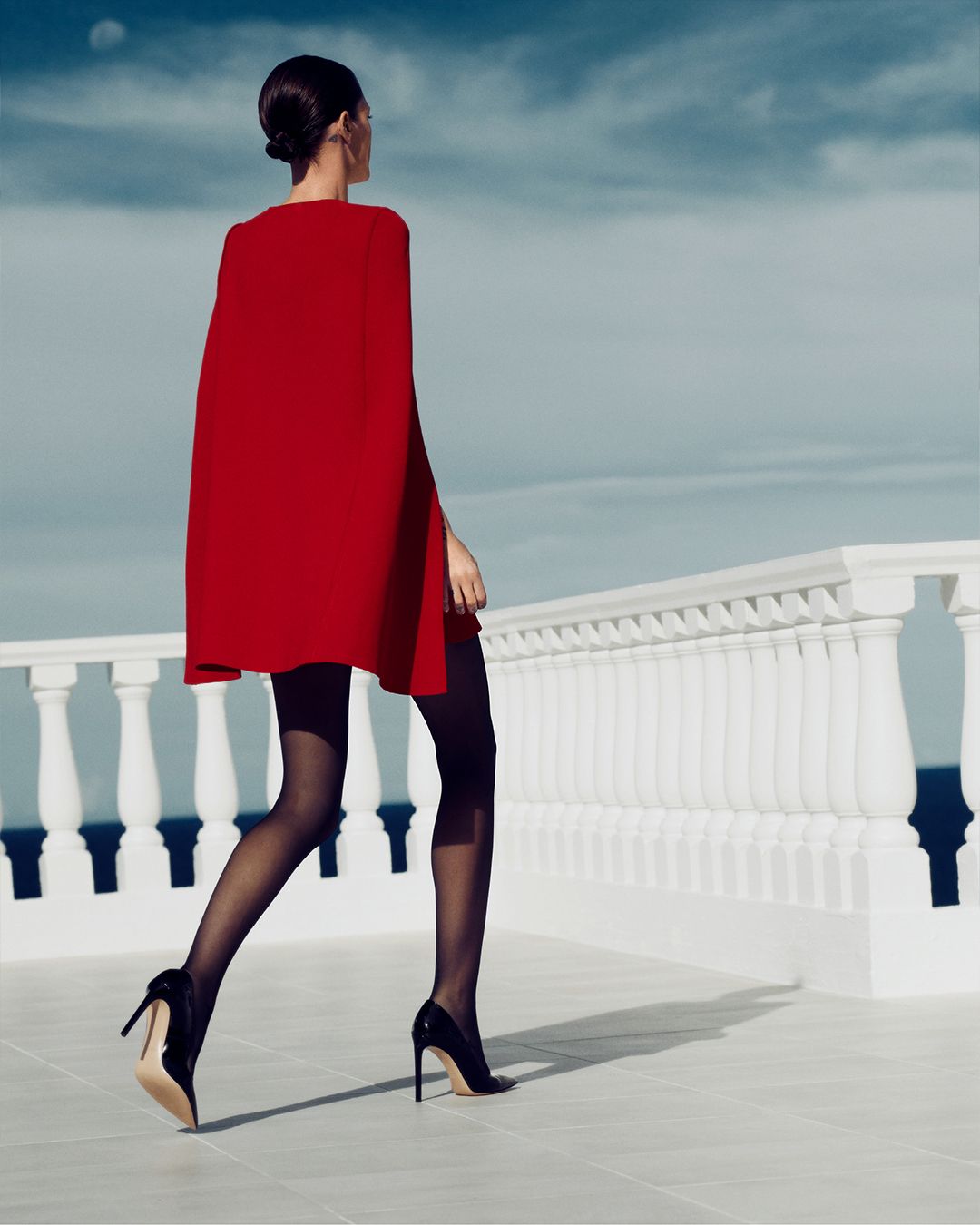 Back view of model in Crepe Knit Red Cape Dress walking toward balcony