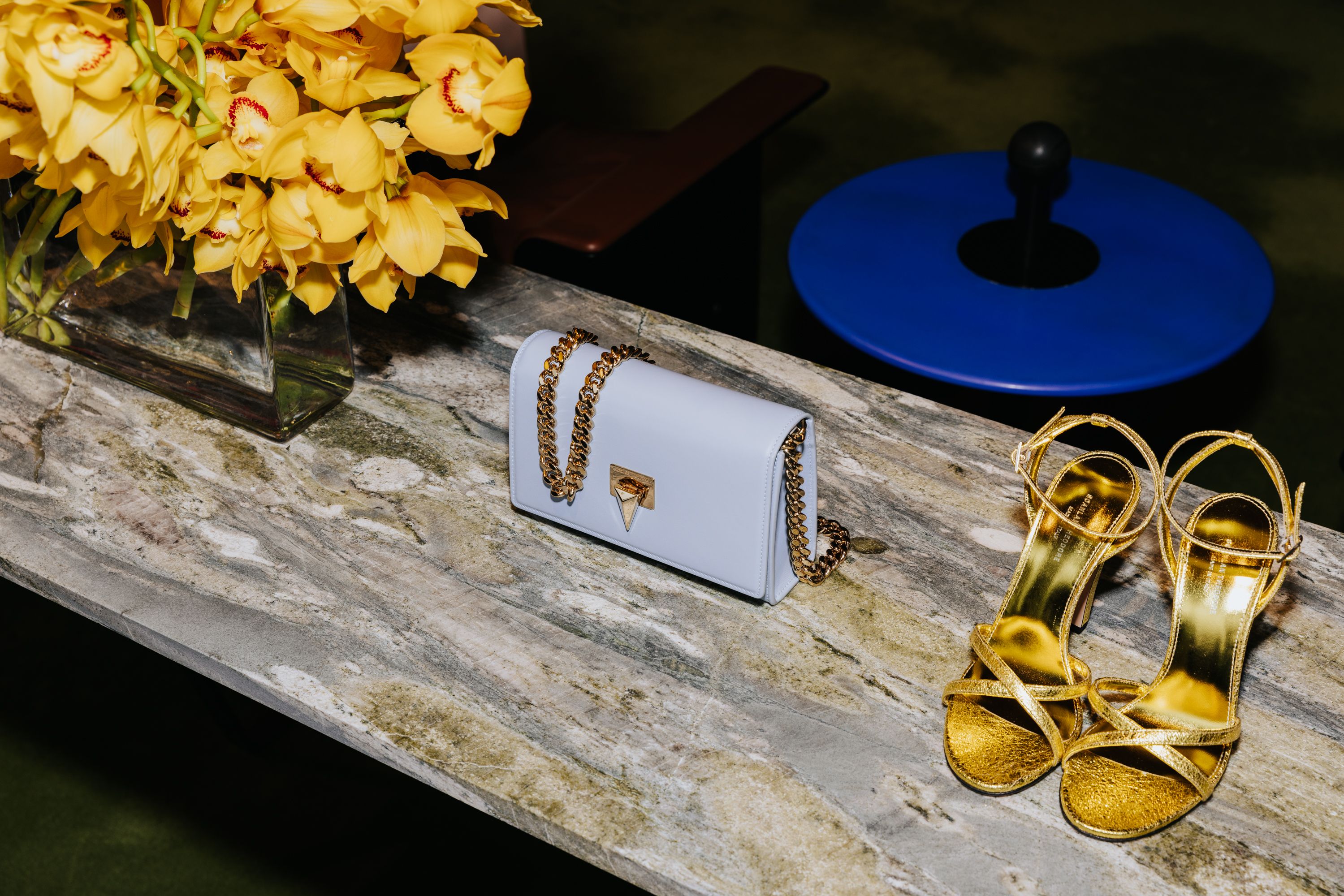Close up of table with yellow flowers, gold strappy heels and a baby blue leather bag