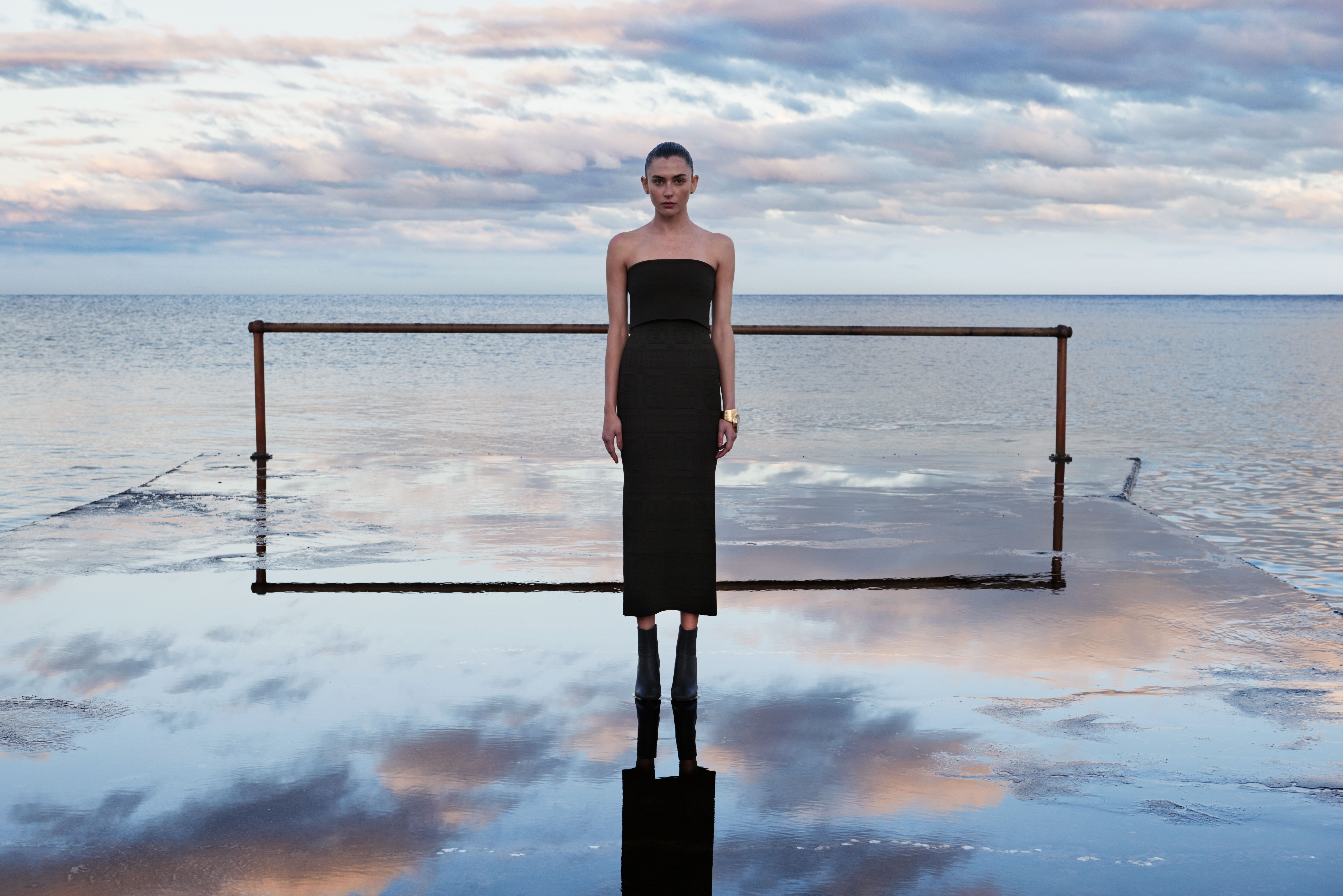 Model standing in front of the ocean wearing a black strapless Crepe Knit dress