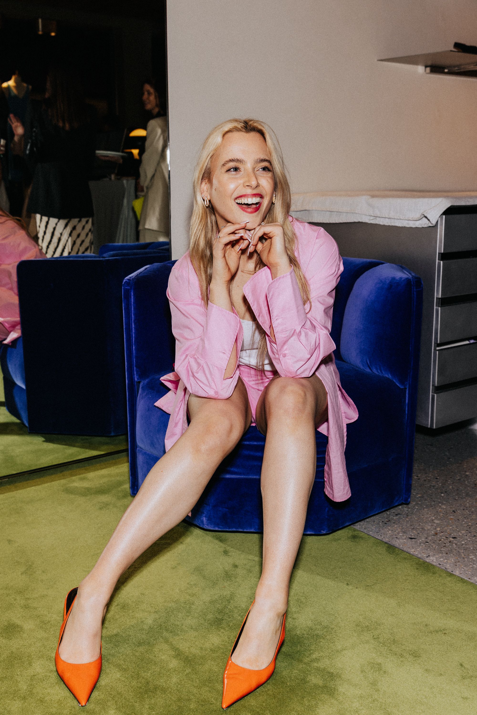 Woman smiling sitting on blue velvet chair wearing pink cotton shirt and shorts
