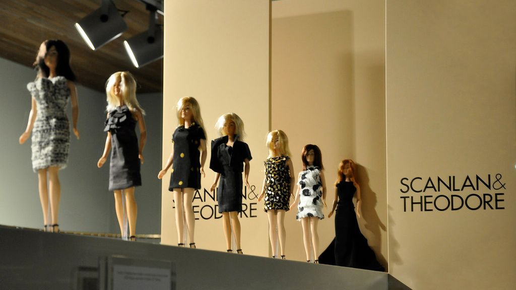 Seven Barbie dolls lined up down a mini runway wearing an assortment of black formal and cocktail dresses
