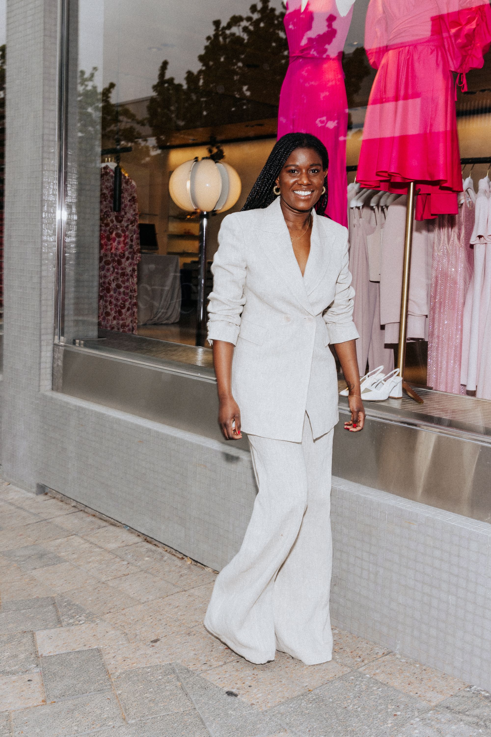Woman smiling standing outside store in white jacket and trousers