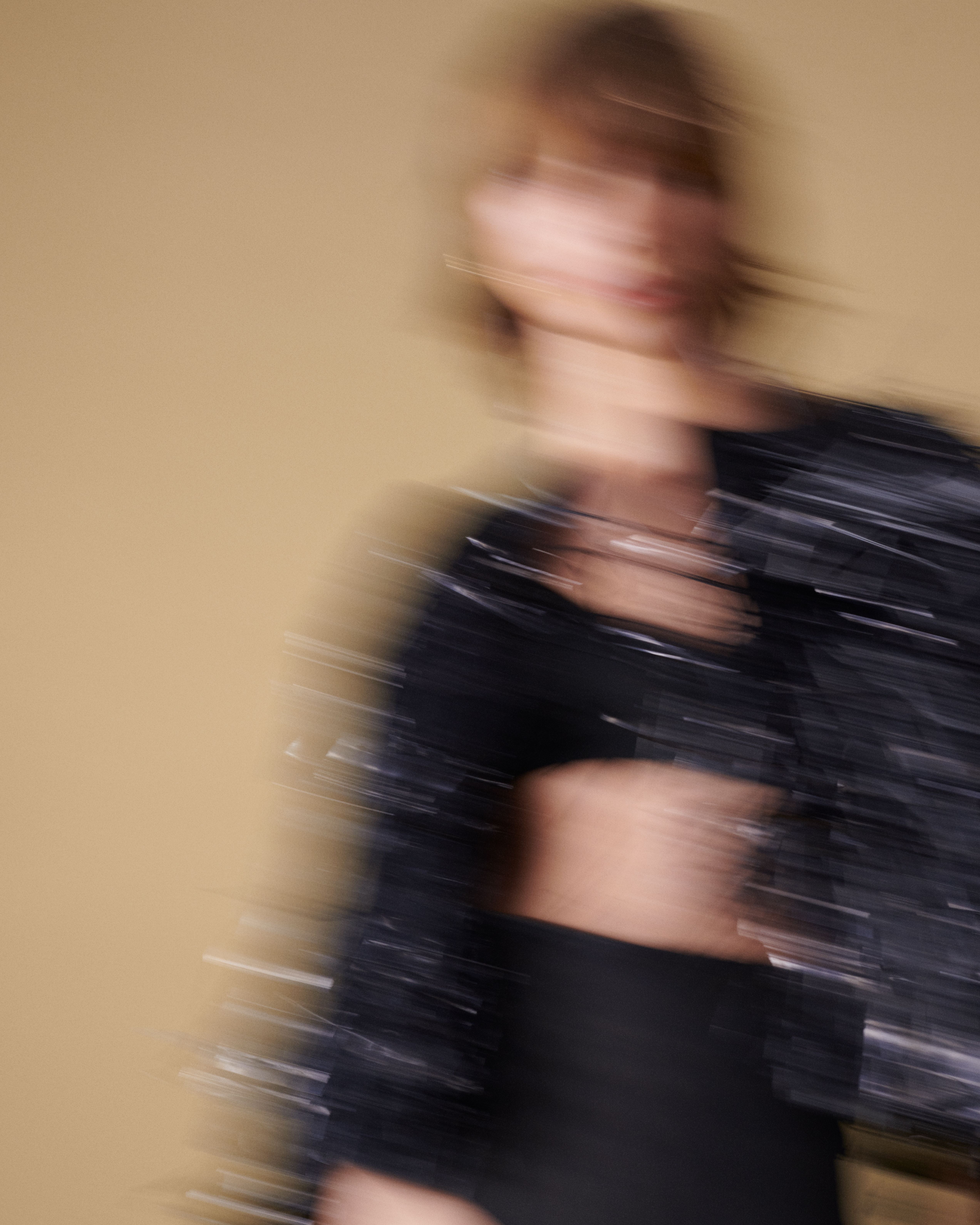 Blurred image of woman moving in a black tinsel fringed jacket, black bralette and underwear
