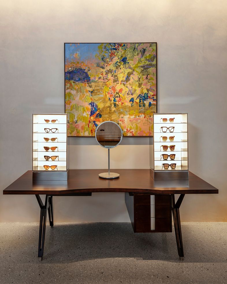 Display sunglasses and a round desk mirror on a table with an abstract painting on the wall behind