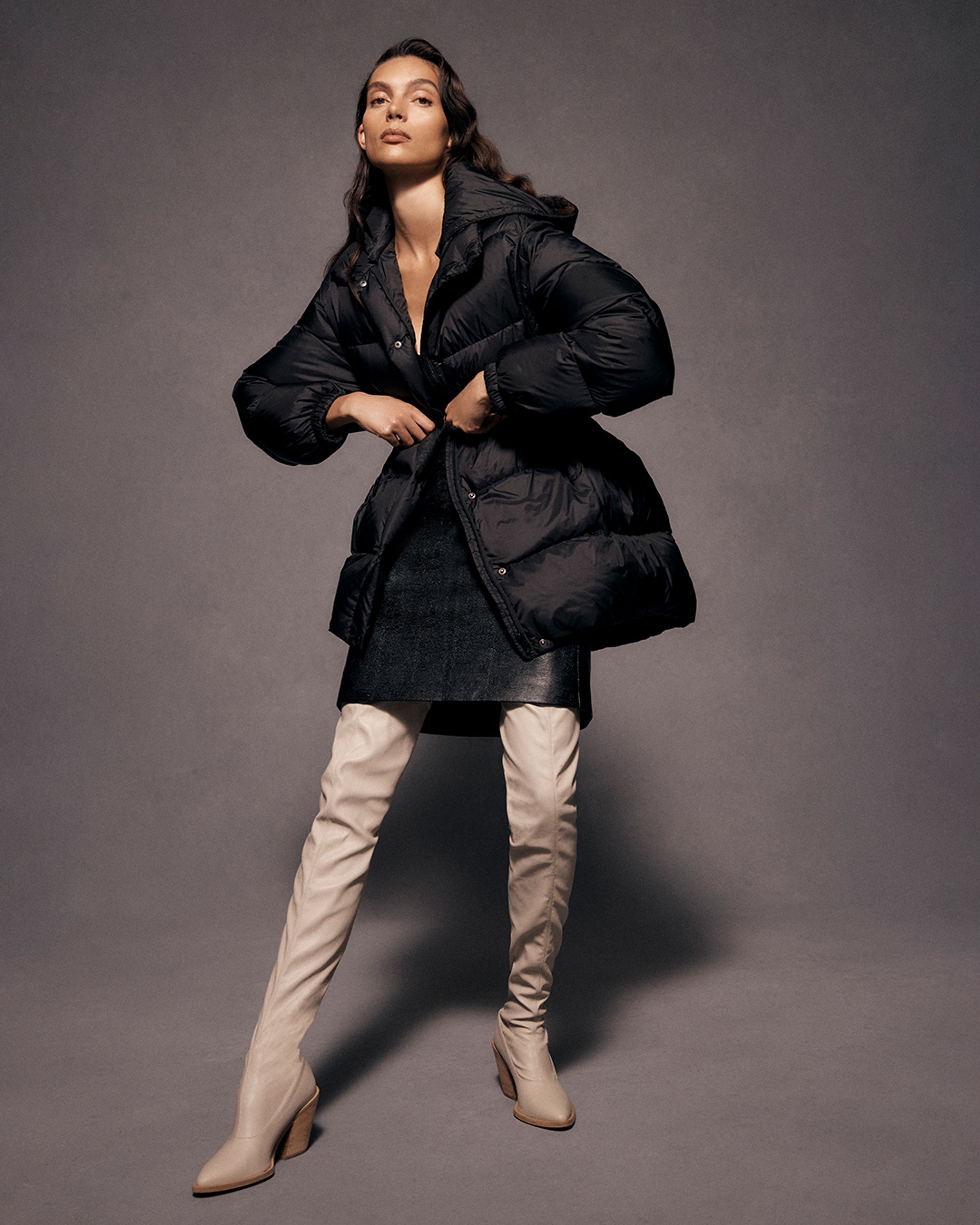 Brunette model standing with arms on waist wearing a black puffer coat and neutral boots