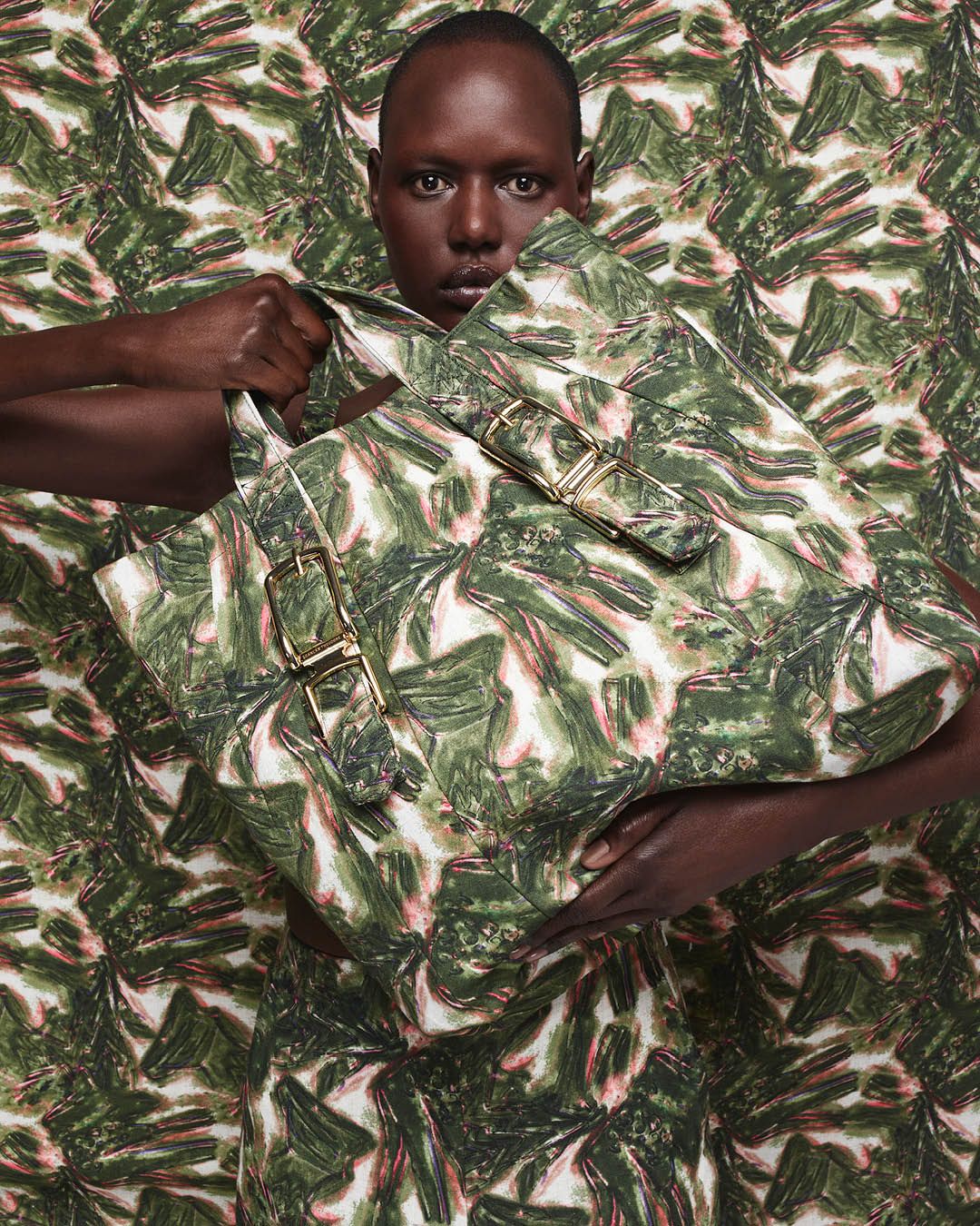 Ajak Deng standing in front of a green tropical print background carrying a large bag with the same print