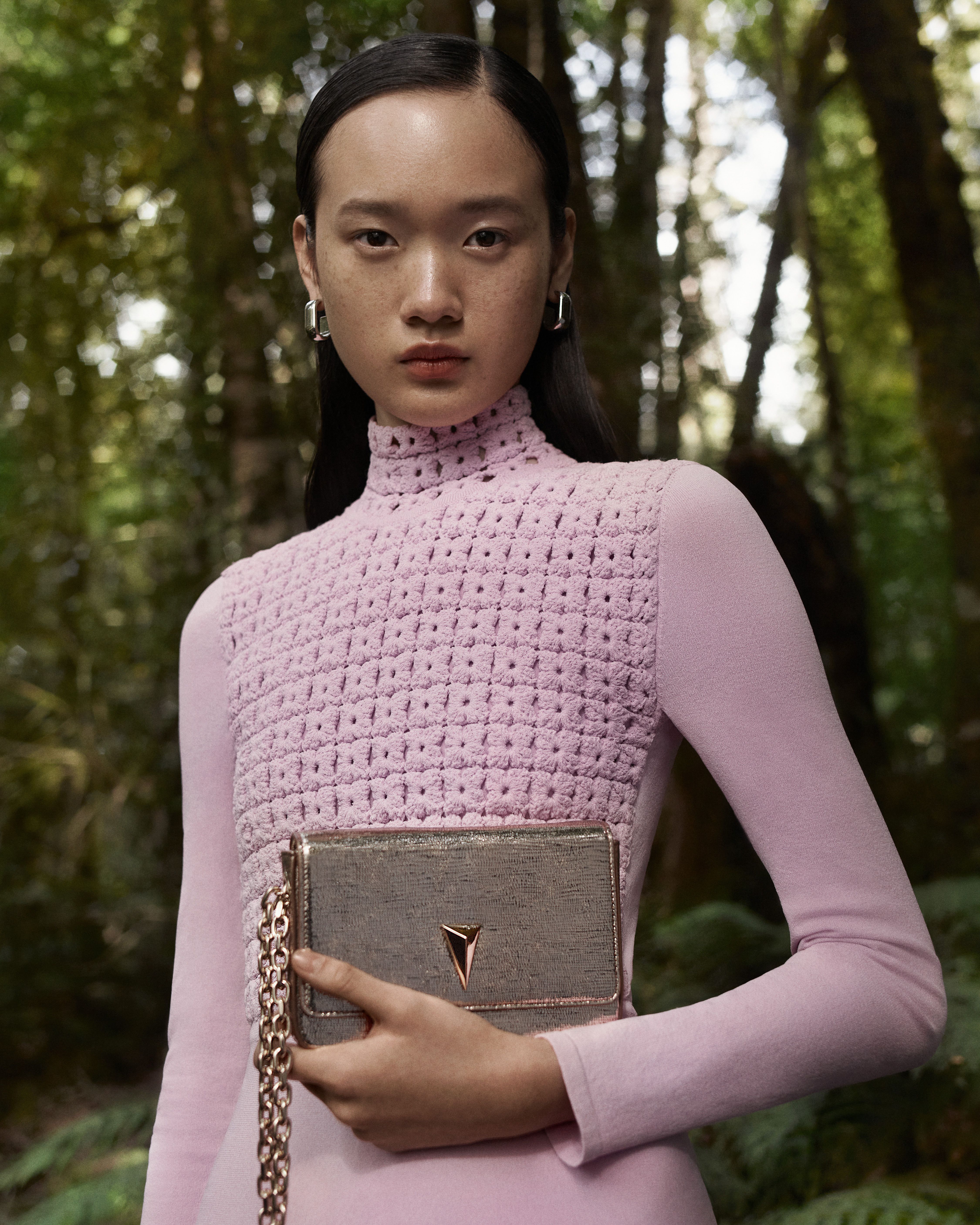 Venus He wearing a pink Crepe Knit long-sleeved dress carrying a gold bag in the forest