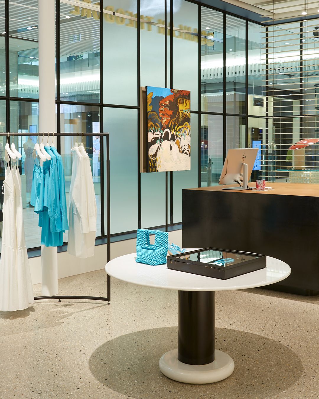 Interior of women's fashion boutique with turquoise and white clothing, a counter and abstract painting