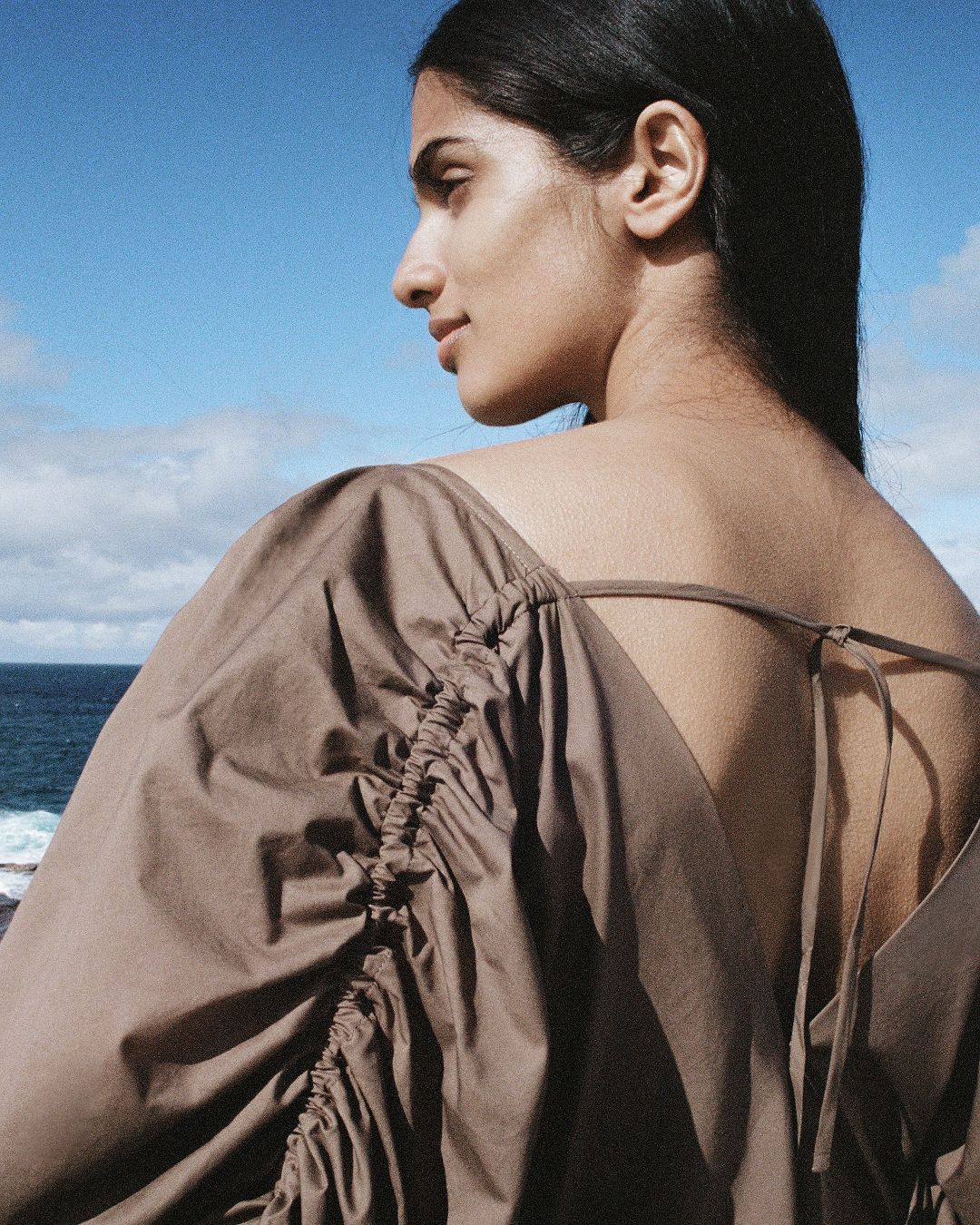 Profile head shot of girl showing tie and gather detail of her brown dress across her back.