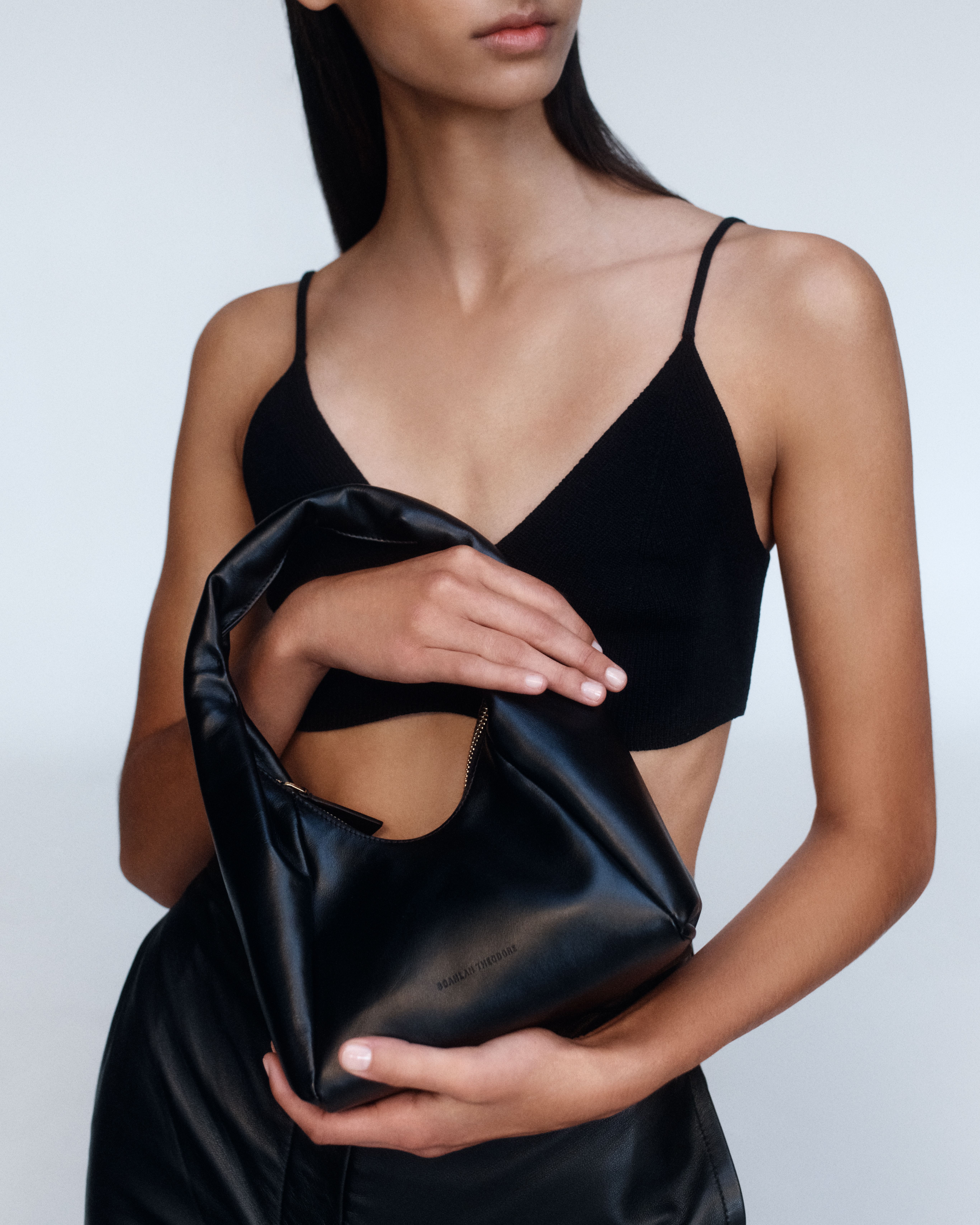 Model holding a small black leather bag wearing a black cropped singlet and leather skirt