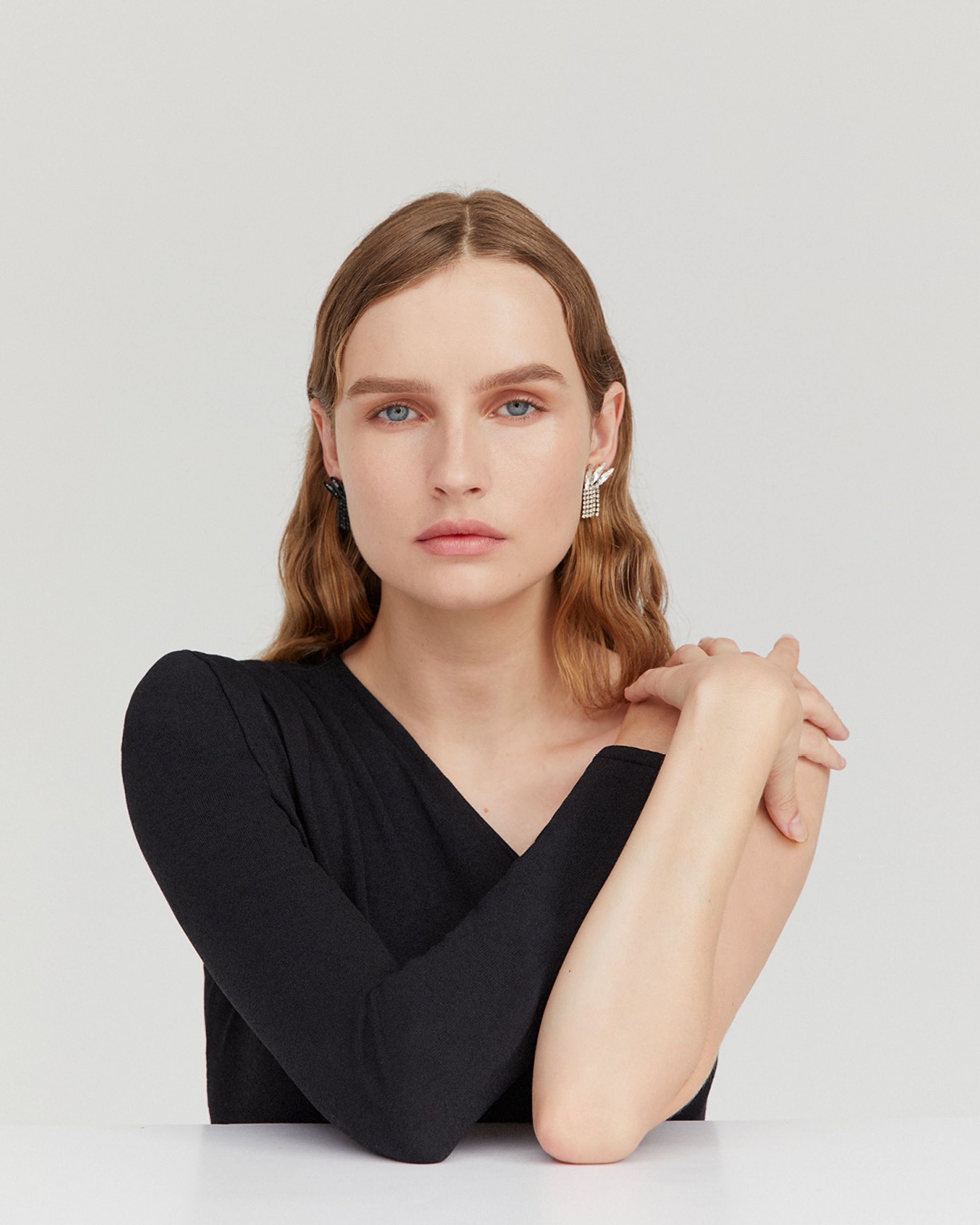 Olivia DeJonge with hands interlaced on her shoulder wearing a black one-shouldered gown