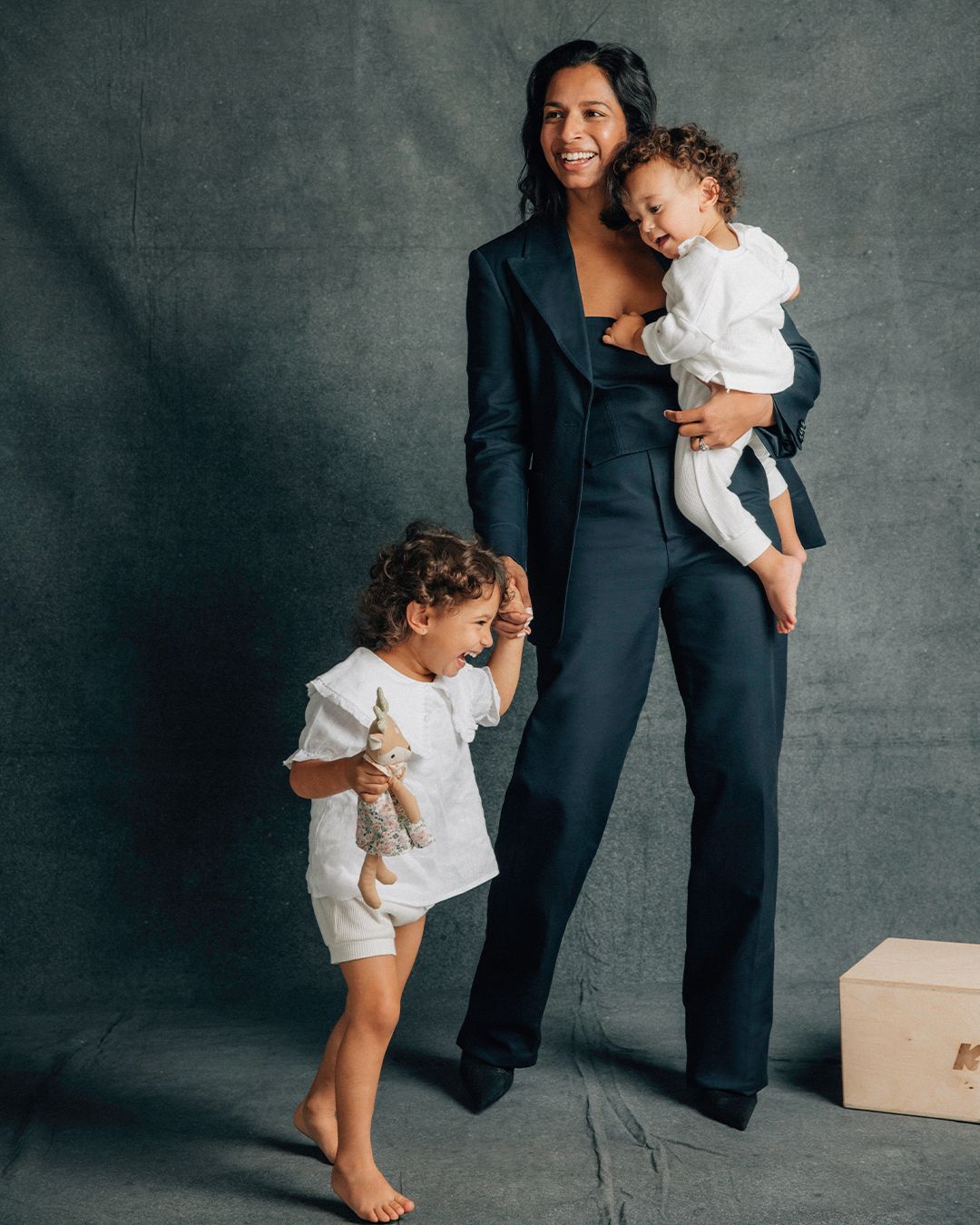 Shamini Rajarethnam smiling wearing a black pant suit holding her son and holding hands with her daughter