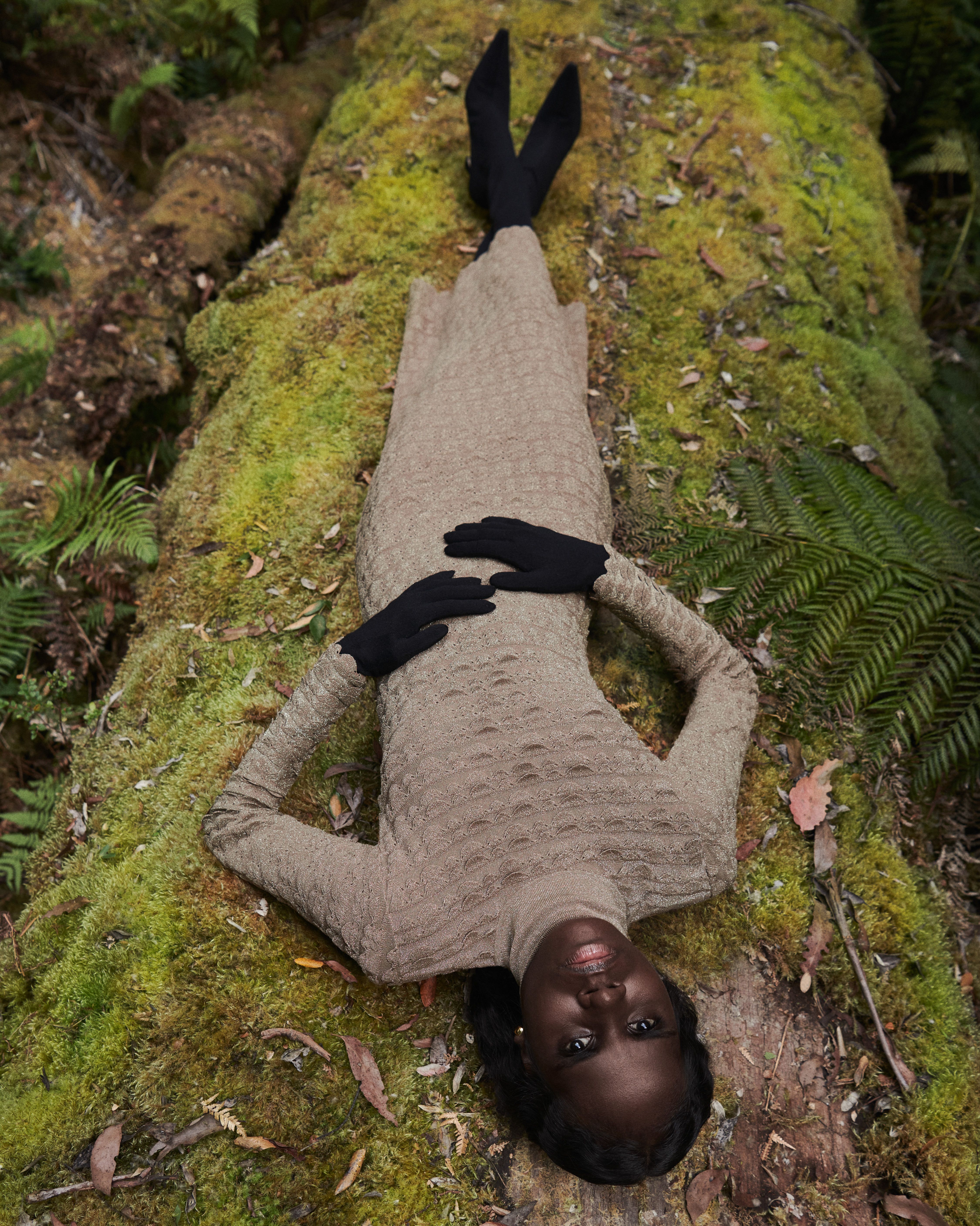 Tarlisa Gaykamangu reclined on moss in the forest wearing a brown knitted gown.