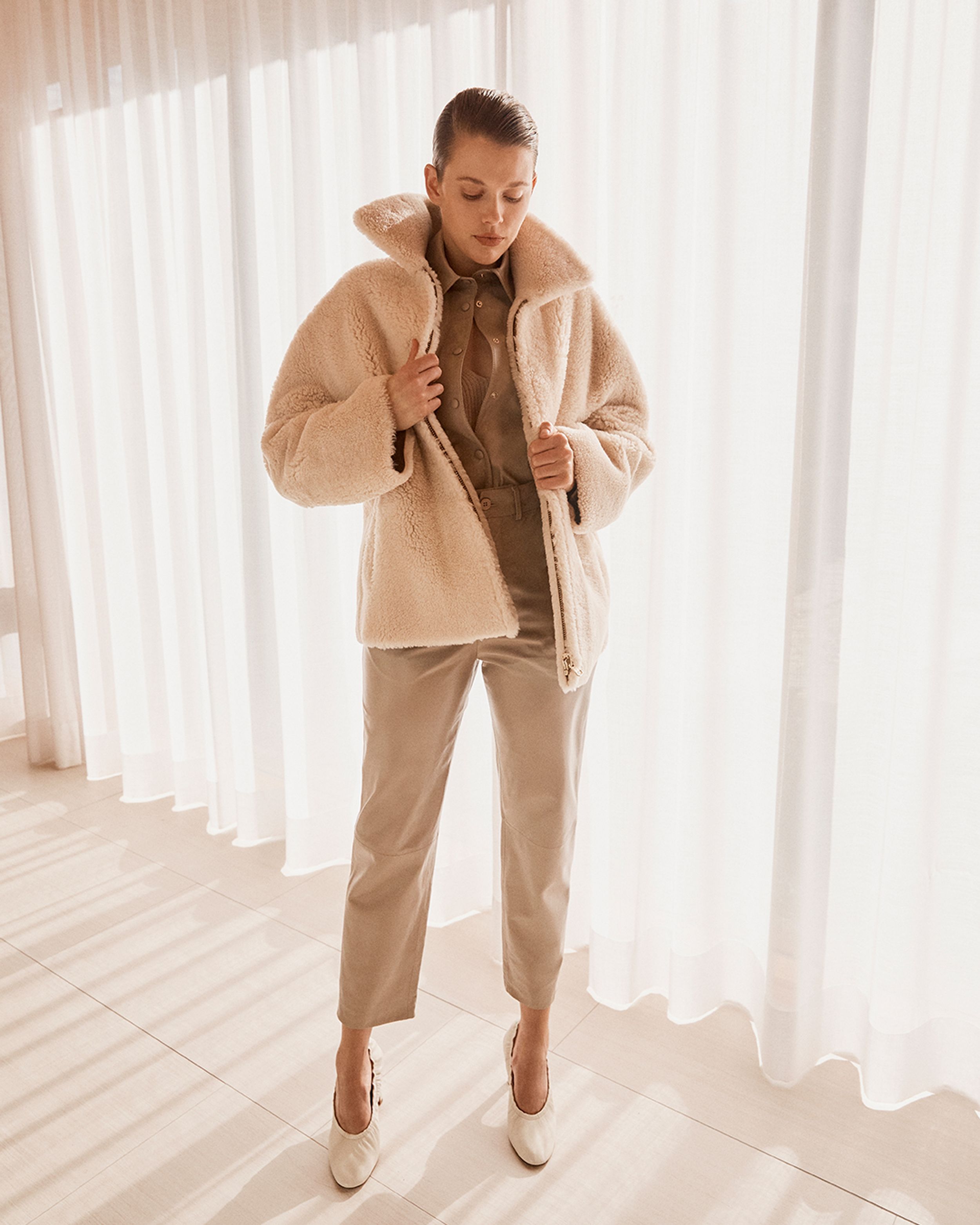 Model standing by window looking down wearing a shearling jacket