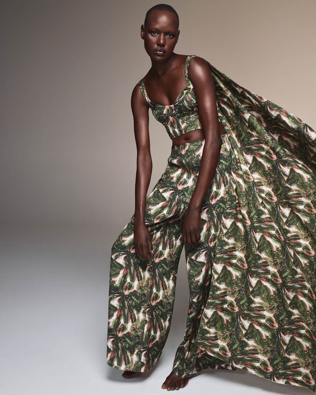 Ajak Deng leaning over wearing a matching green tropical print bustier and trousers