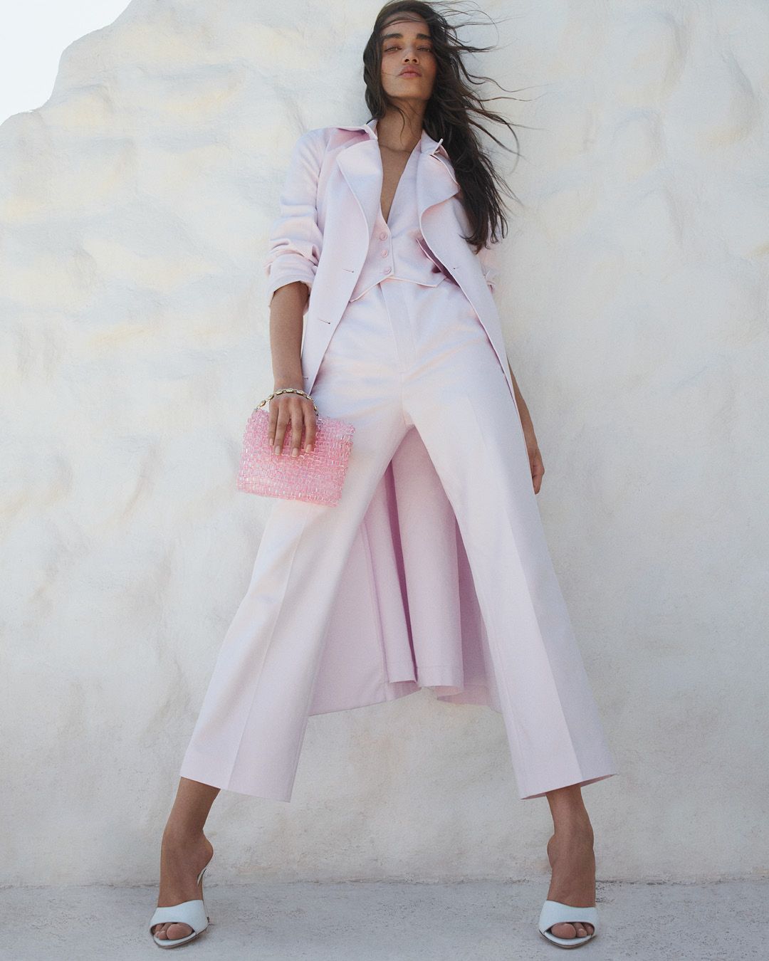 Model standing wearing a baby pink trench coat, trousers and beaded bag