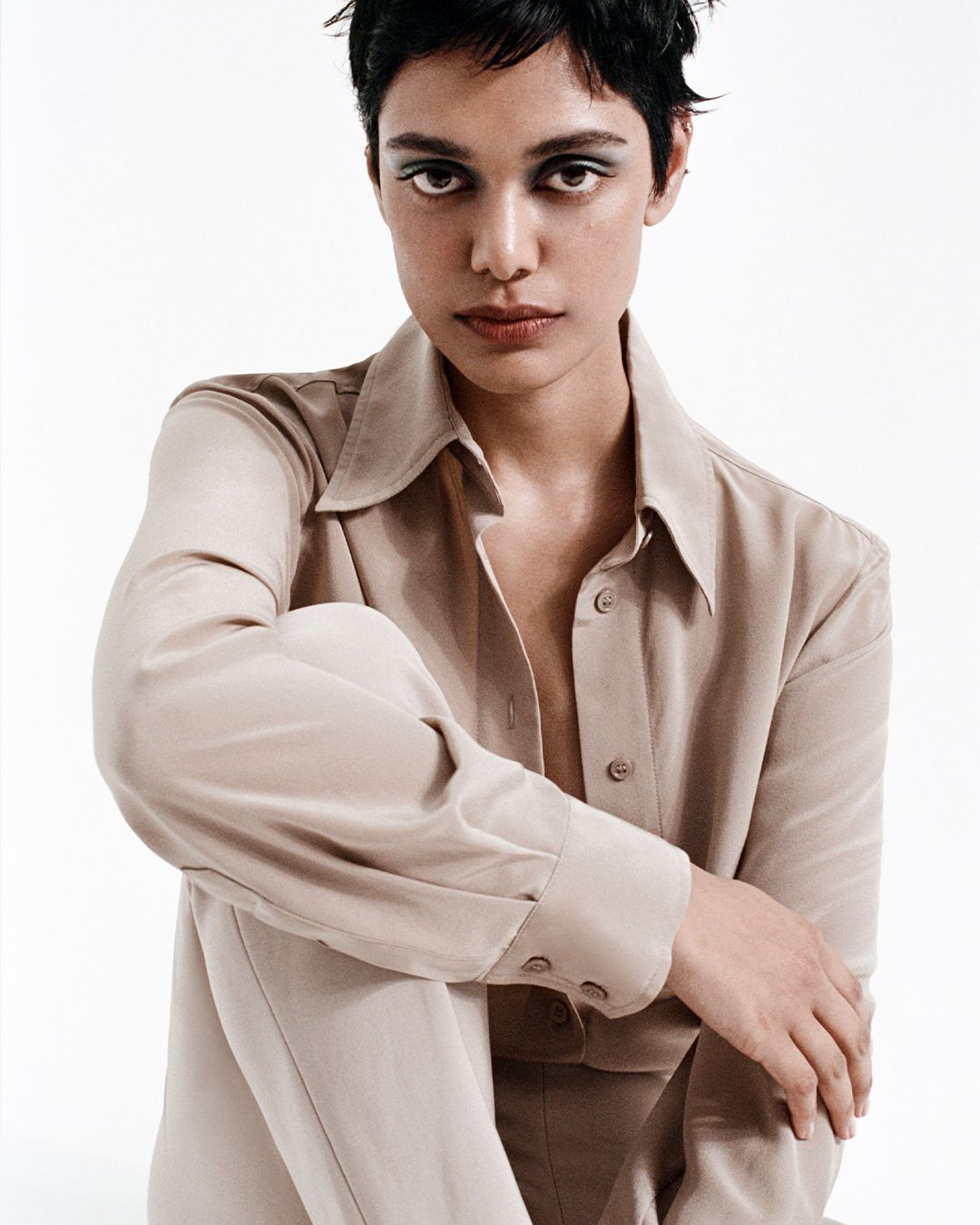 Zinnia Kumar sitting with her arm on knee in a taupe silk blouse