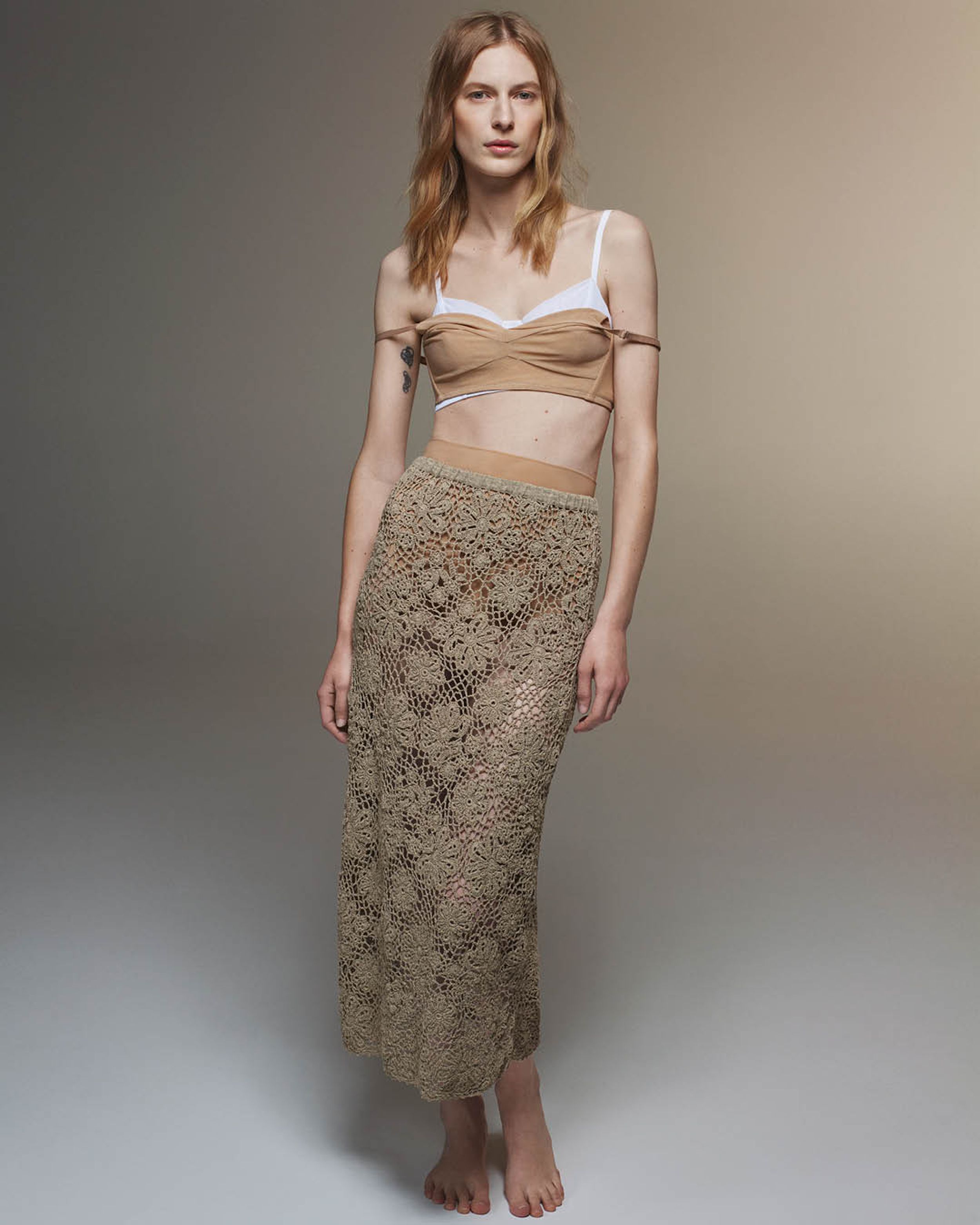 Julia Nobis wearing a beige mesh bra layered over a white mesh bra and taupe crocheted long skirt