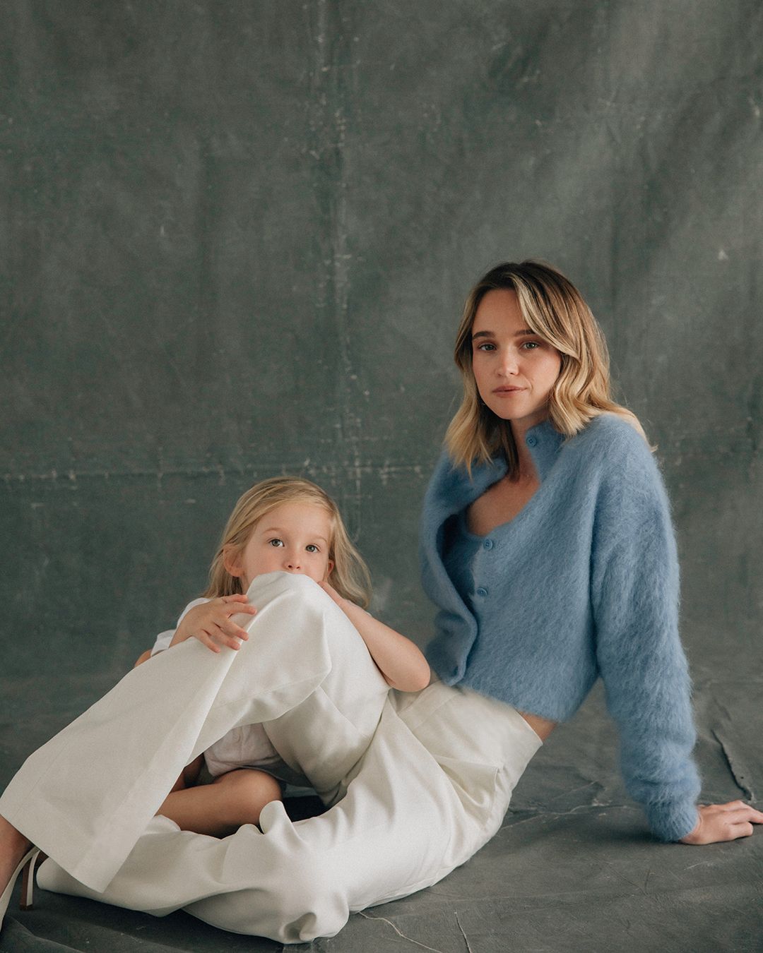 Rosie Tupper sitting on the ground wearing a blue mohair cardigan and white trousers with her 3 year old daughter