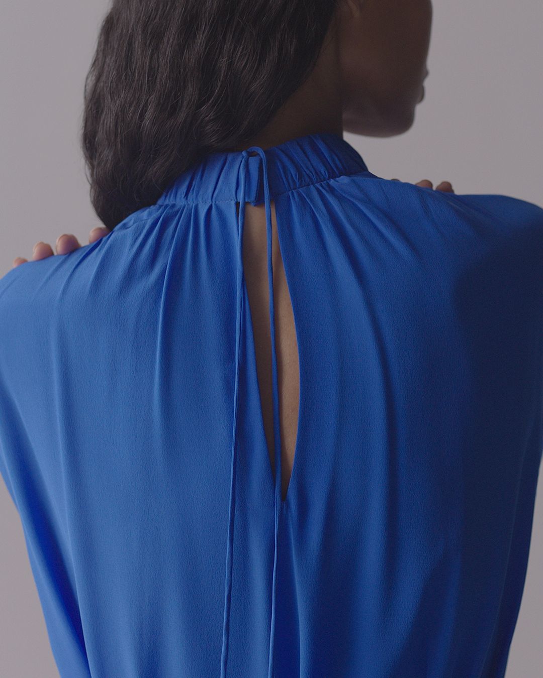 Close up of back of cobalt blue dress, cut out showing woman’s skin. Fingers on top of shoulders. 