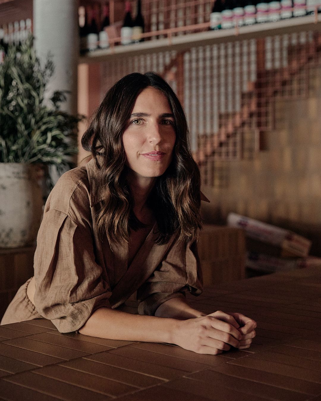 Bianca Marchi leaning over a brown tiled bench wearing a brown linen shirt