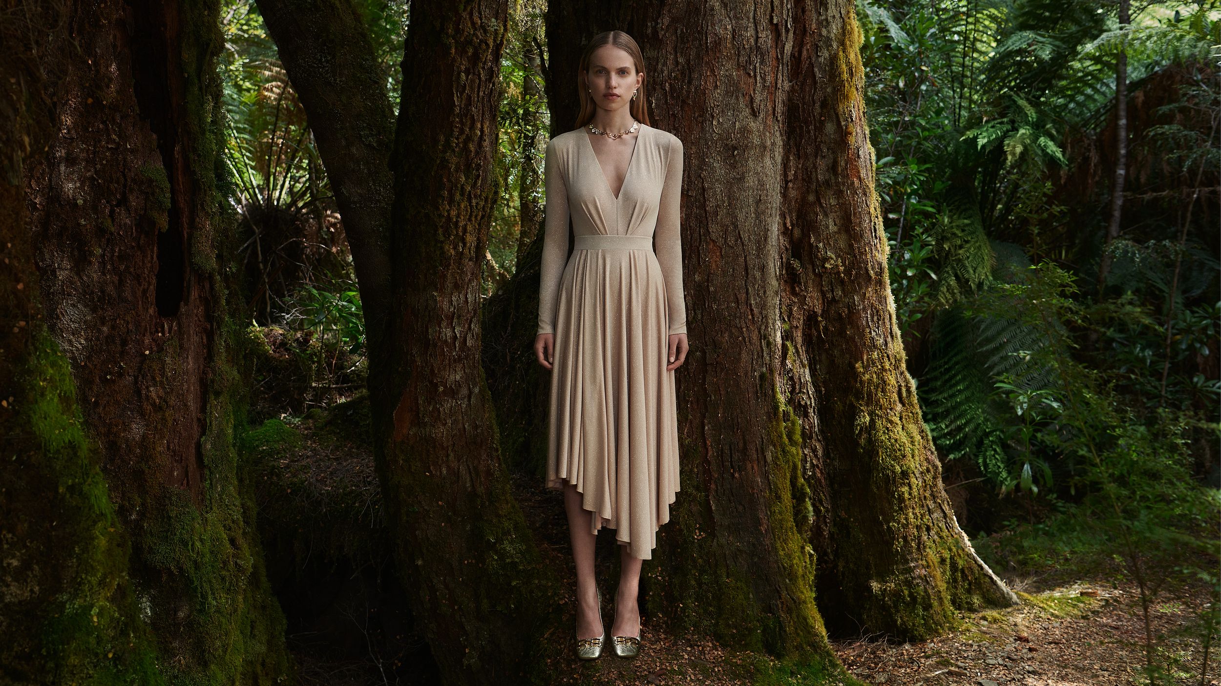 Sabine Glud standing in the forest wearing a beige v-neck top and skirt.