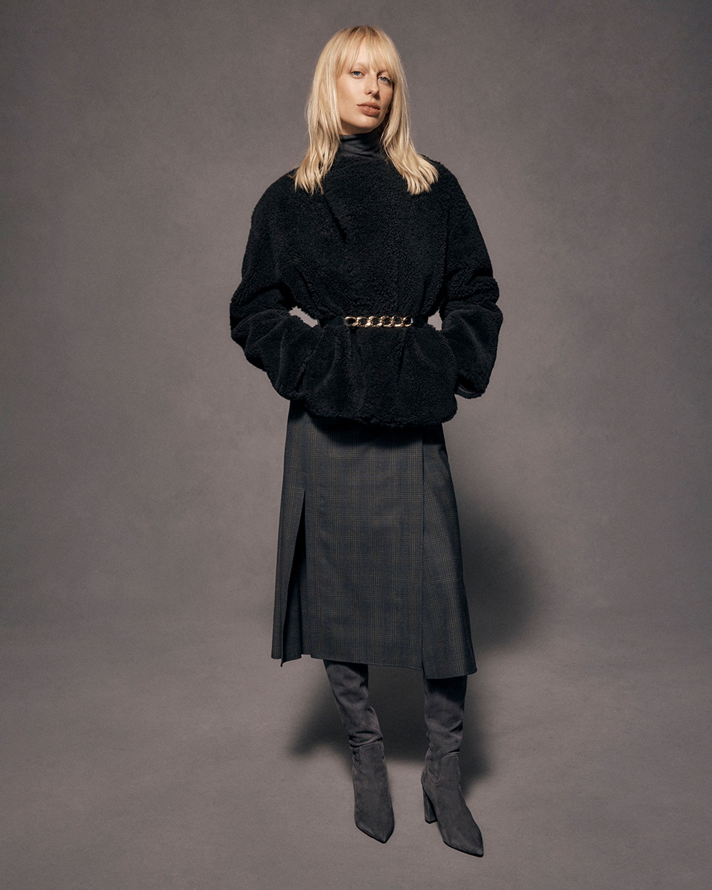 Blonde model wearing a black sweater and grey plaid skirt