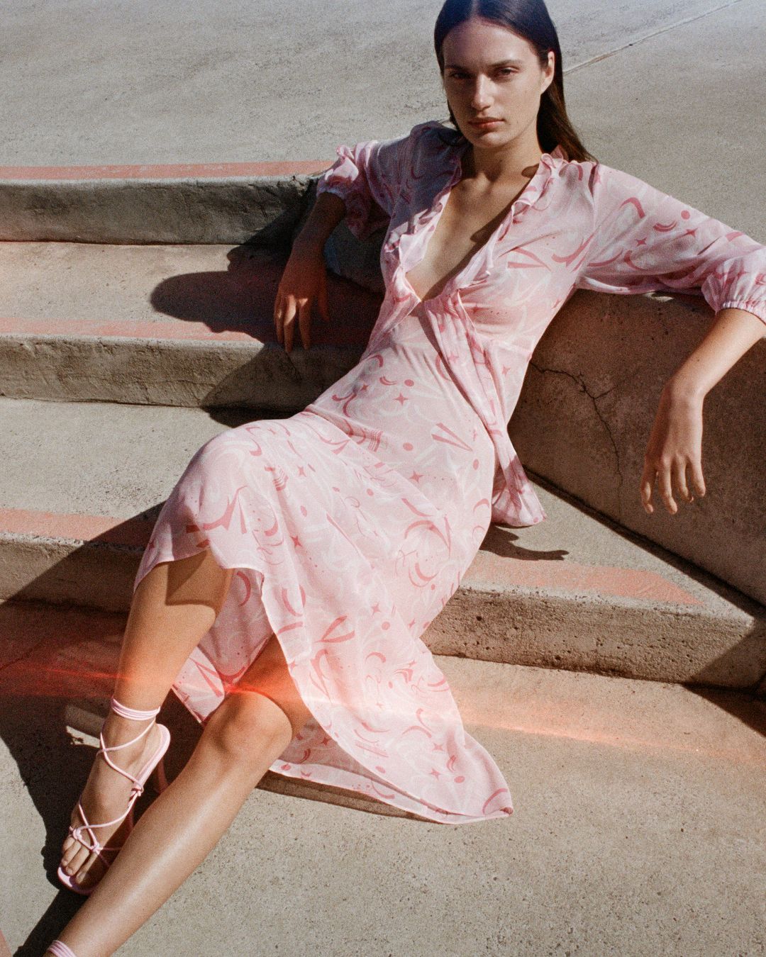 Girl laying on concrete stairs with pink painted lines with one knee bent in pink dress and shoes. 