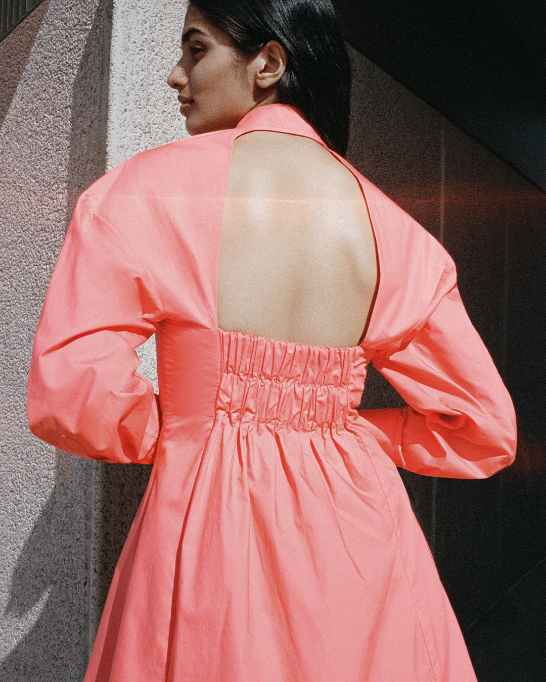 Back shot of girl looking to the side with bent arms crossed in front with open back orange dress.  