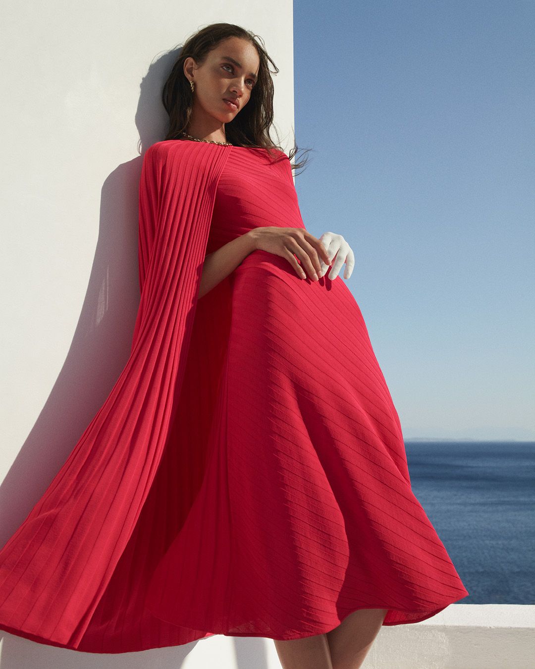 Model leaning against a wall wearing a bright pink dress with the ocean in the background