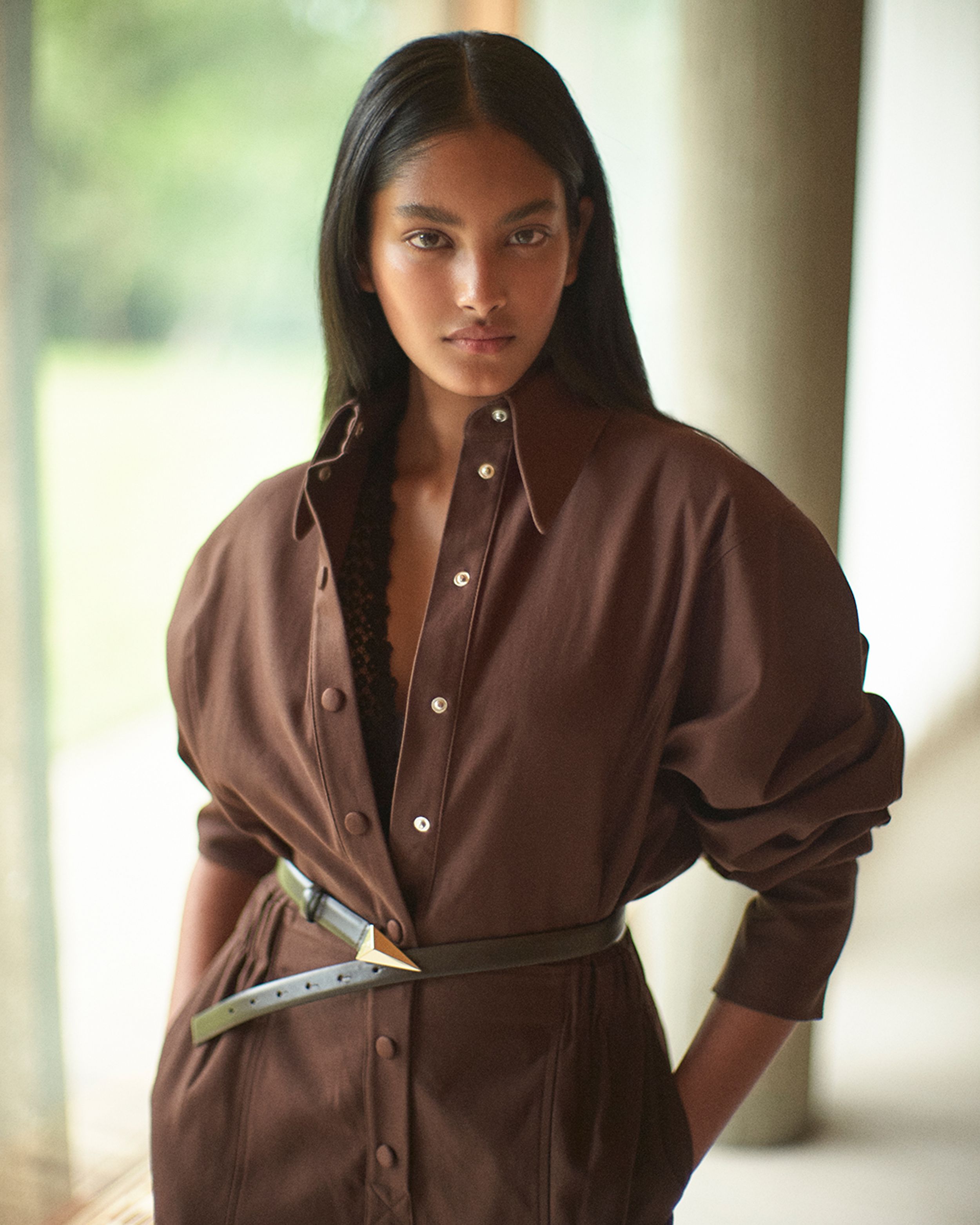 Brunette model posing with hands in pockets wearing a brown jumpsuit and belt